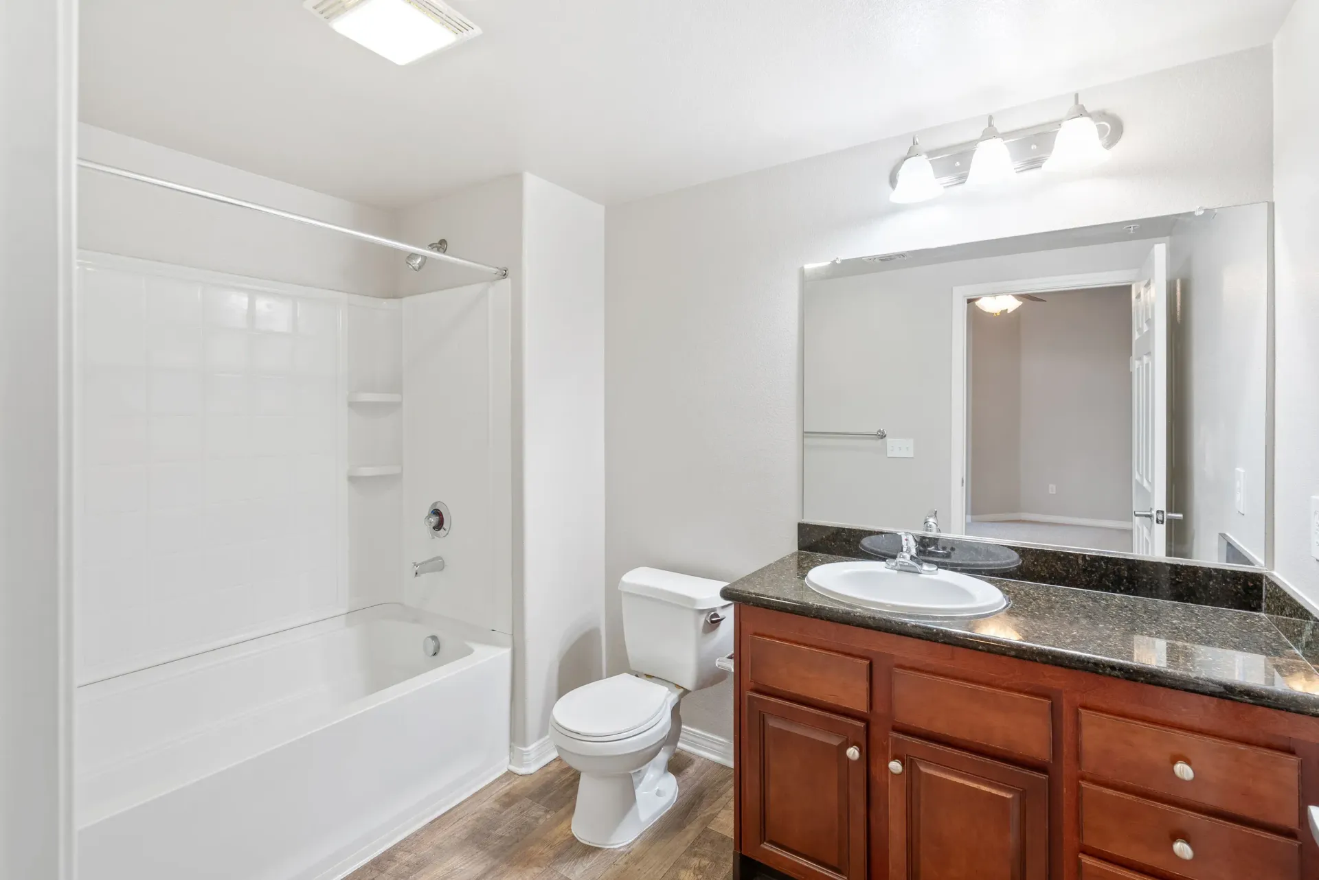 Bathroom with white-tiled tub/shower, toilet, and dark granite vanity.