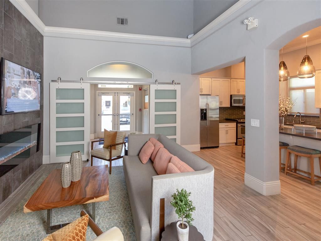 Open-concept lounge with a gray sofa, coffee table, and adjacent kitchen in a clubhouse.