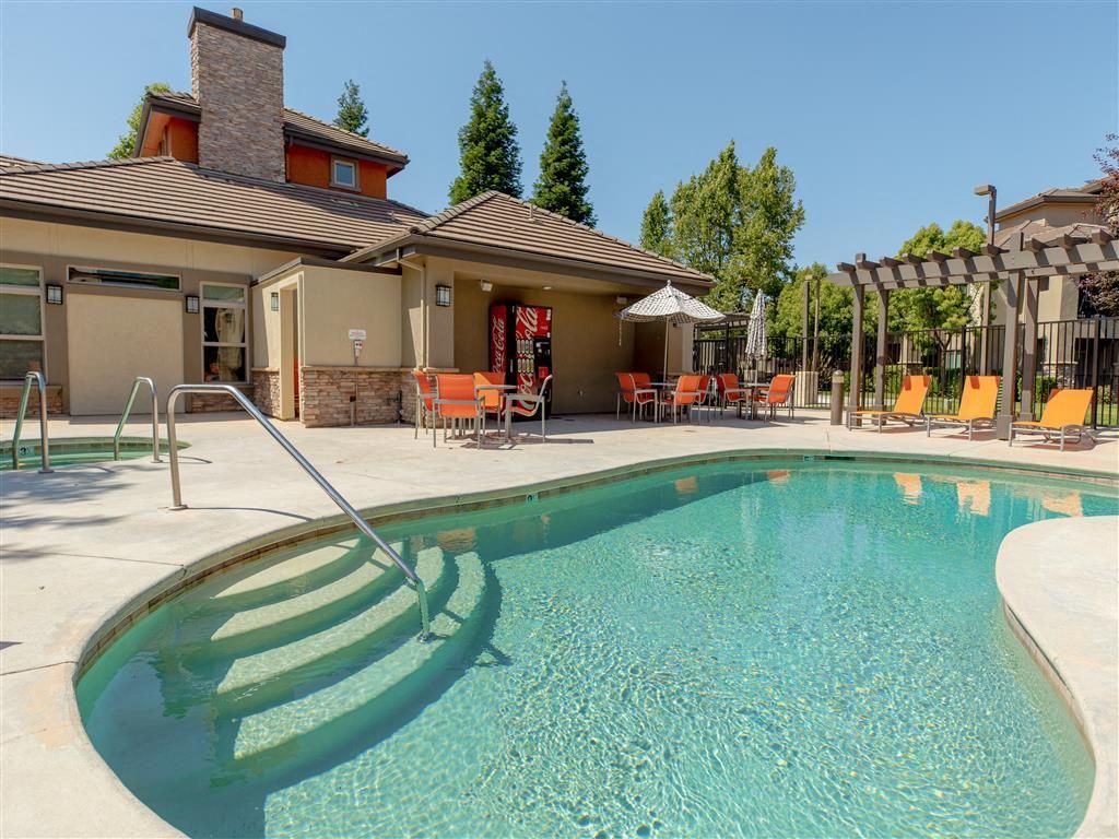 Outdoor pool at an apartment community with lounge chairs, umbrellas, and a shaded patio.