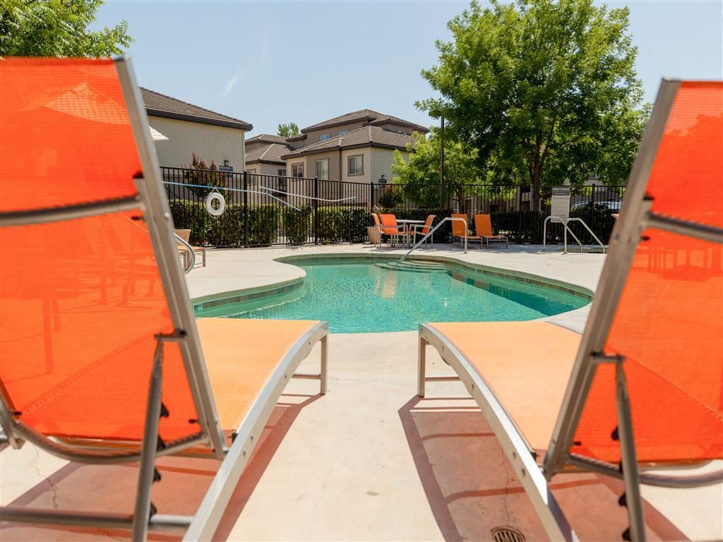 Outdoor apartment pool with orange lounge chairs and surrounding fence.