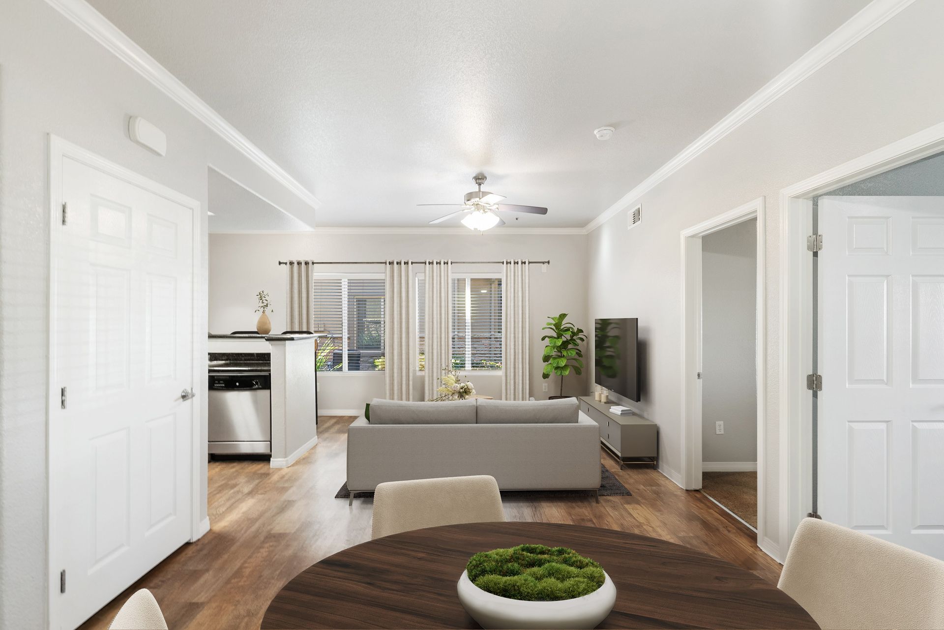 Open-concept living room with gray sofa, TV, dining table, and kitchen area in a modern apartment.