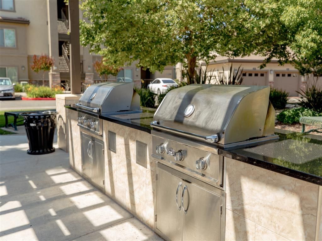 Outdoor grilling station with two built-in stainless steel grills along a stone counter.