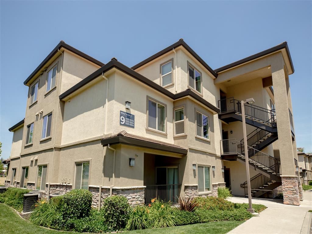 Exterior view of a beige, multi-story apartment building with external staircases.