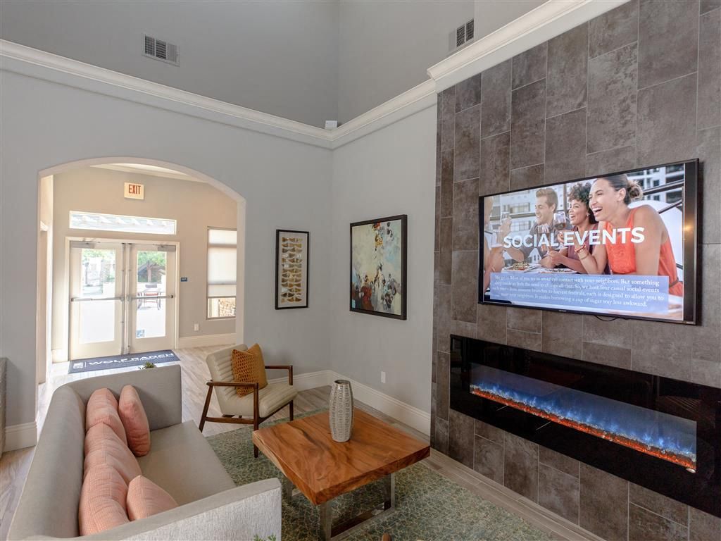 Indoor resident lounge with sofa, chair, coffee table, fireplace and wall-mounted TV.
