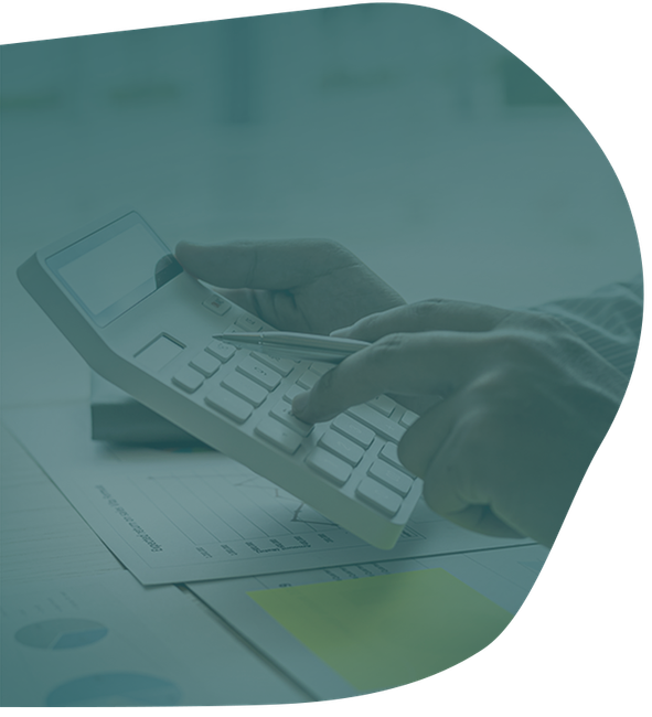 A person’s hands using a white calculator over a document with charts and a yellow sticky note.