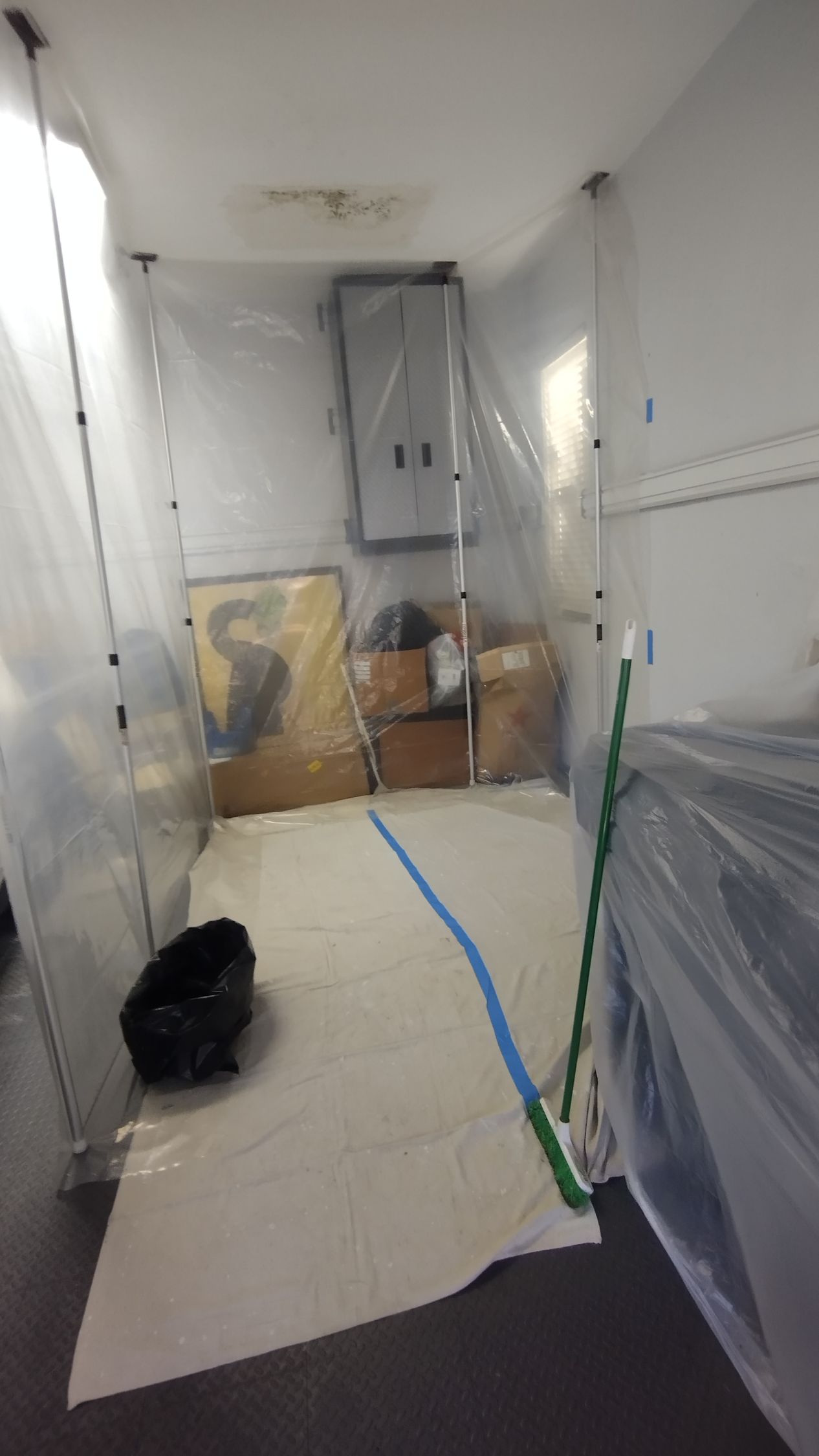 A room is covered in plastic and has a trash can on the floor.