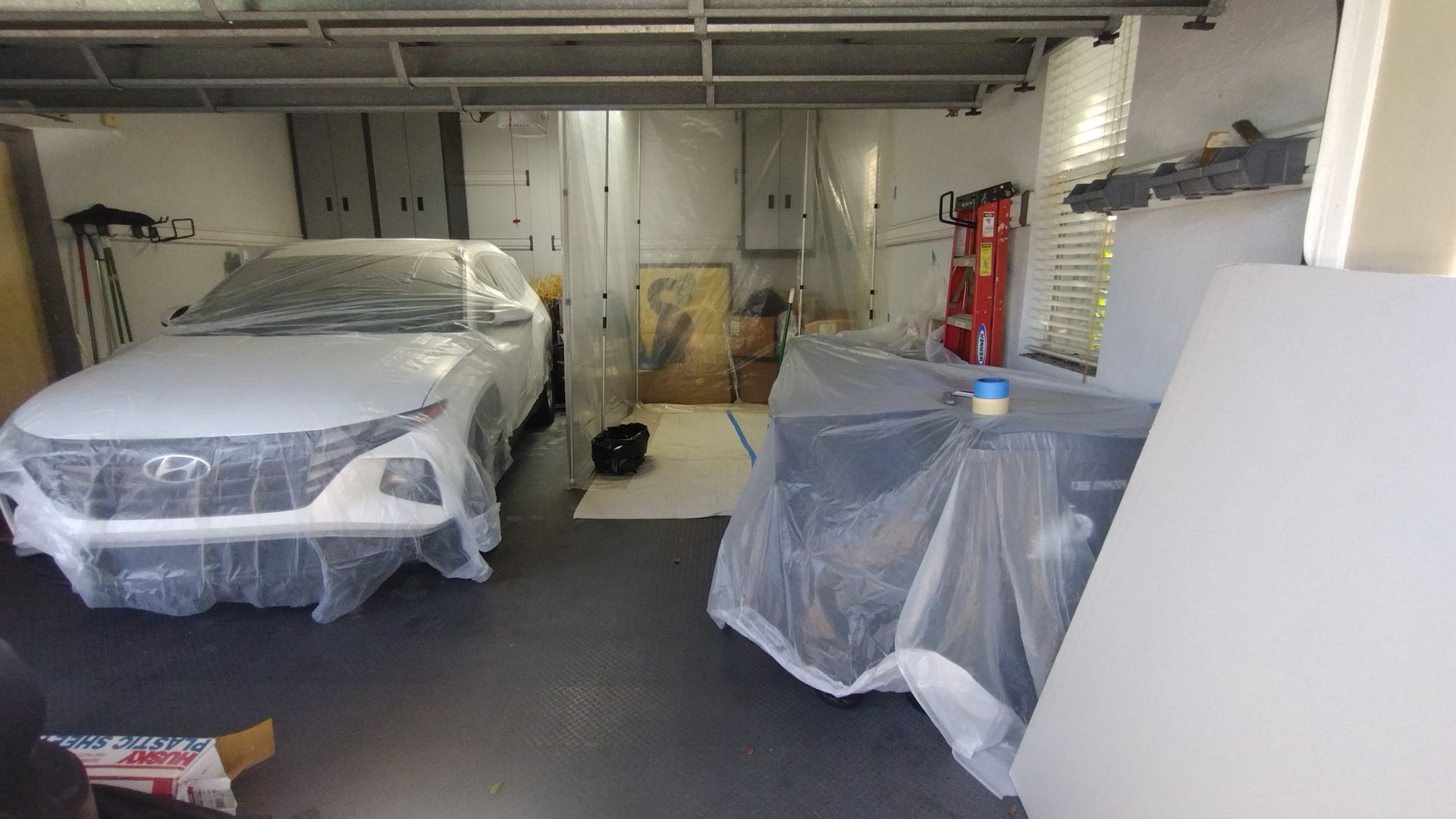 A car is wrapped in plastic in a garage.