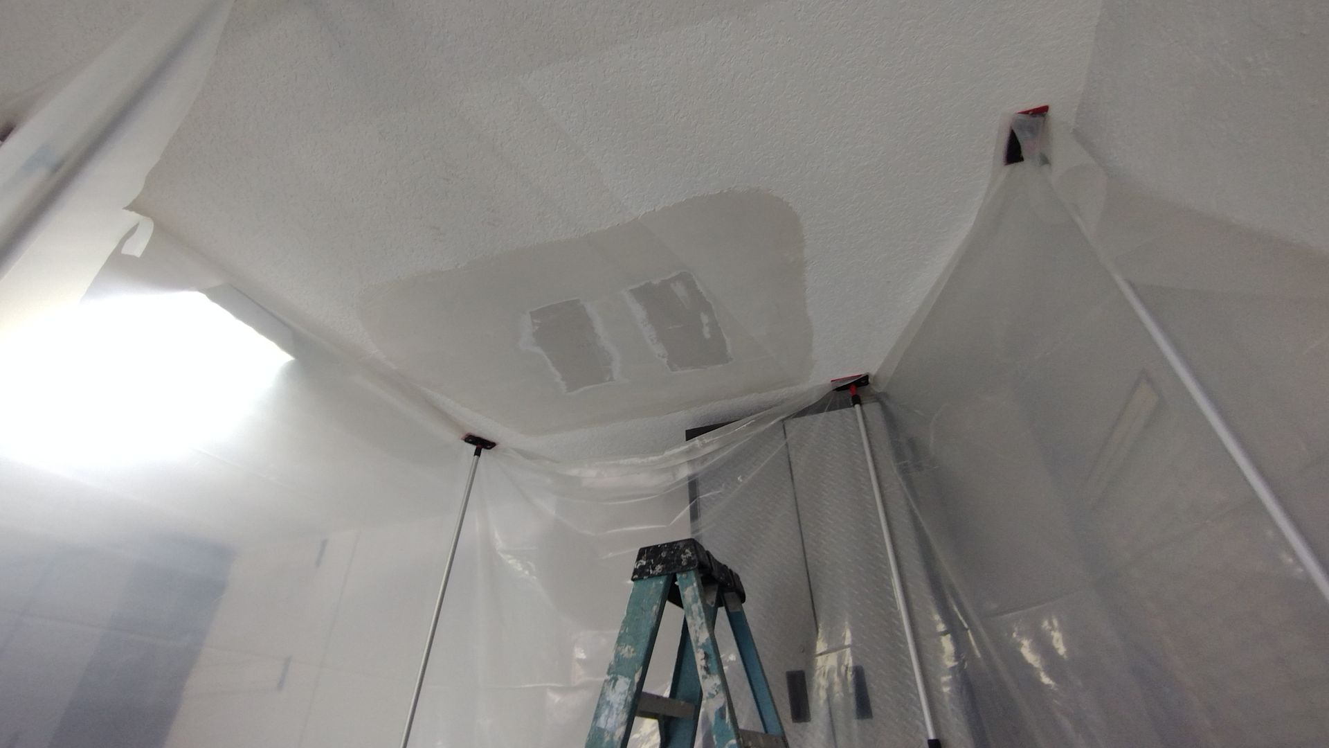 A ladder is hanging from the ceiling of a room covered in plastic.