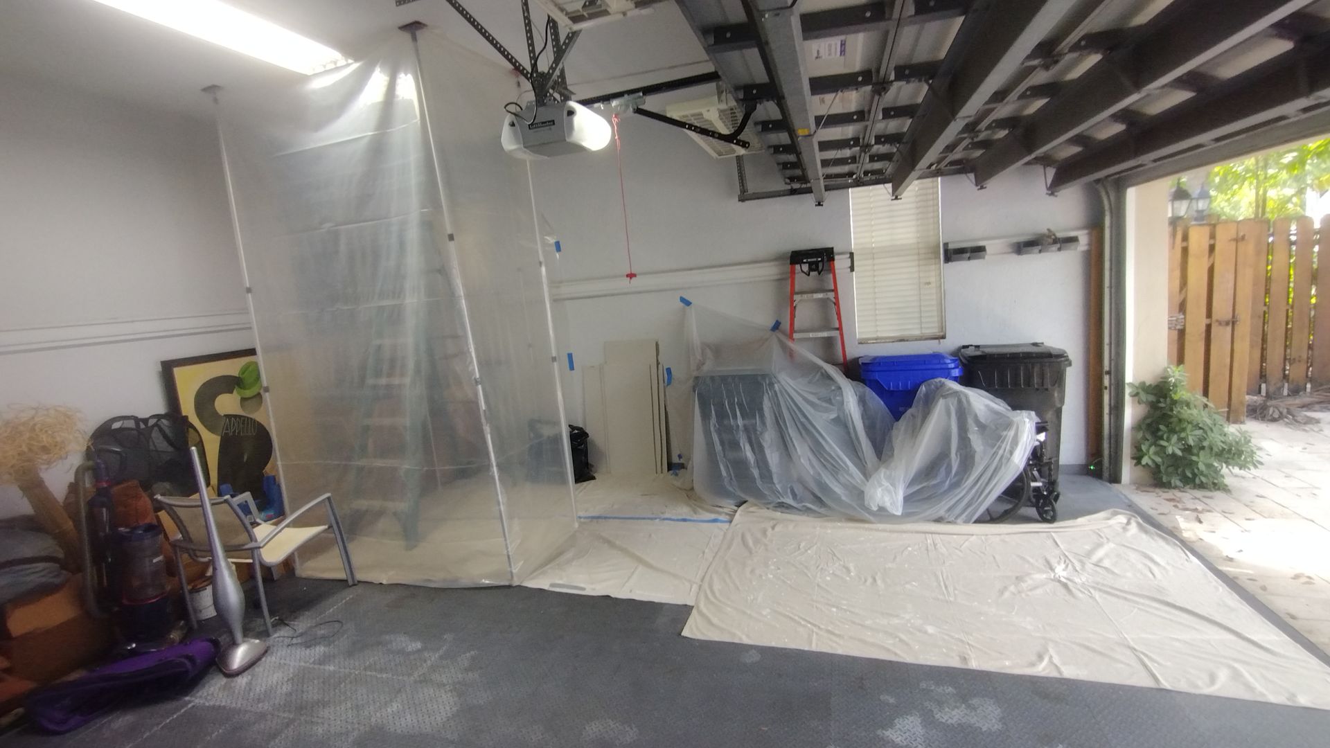 A garage with a ladder and a clear plastic sheet on the floor.