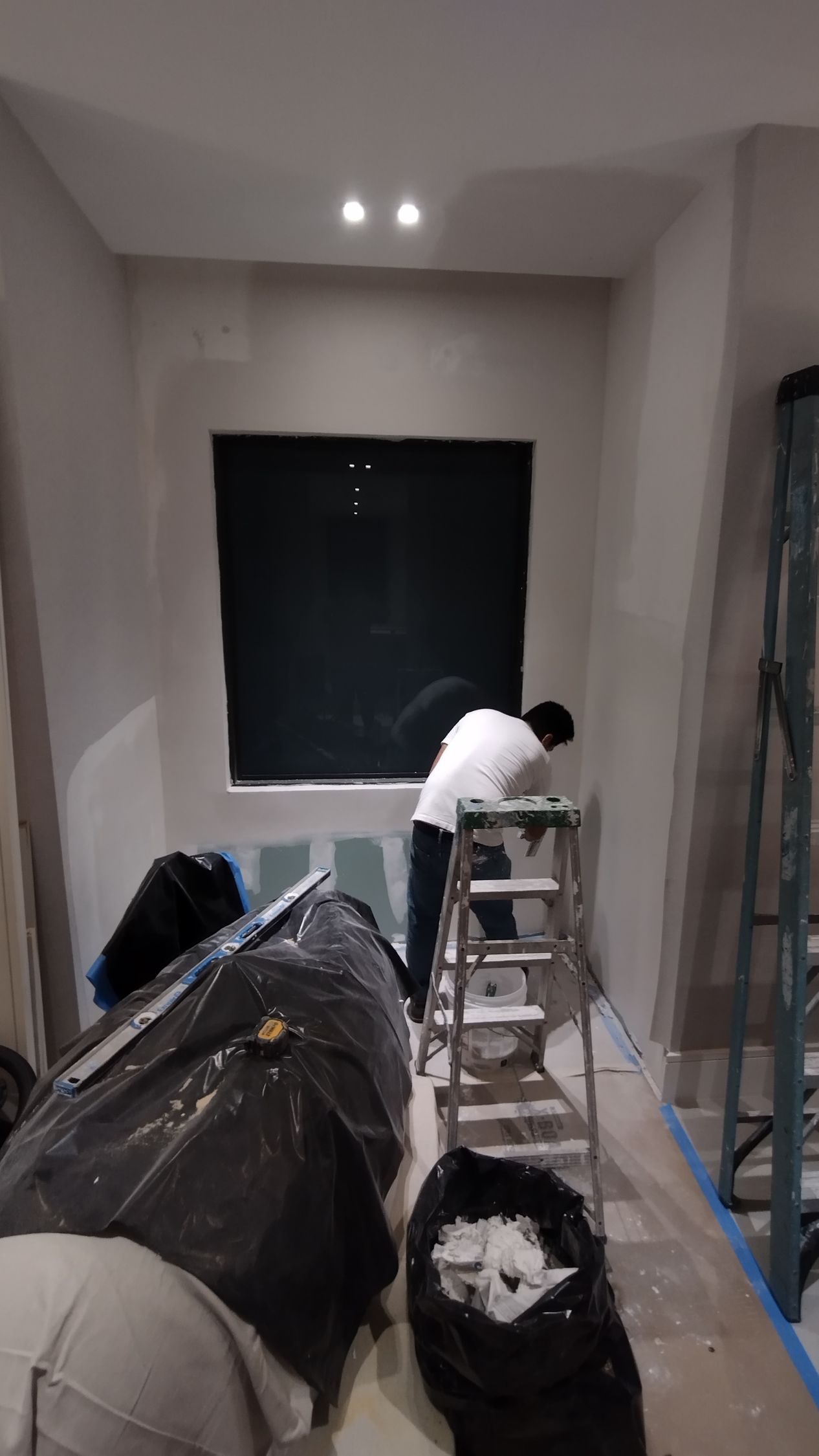 A man is painting a wall in a room with a ladder.