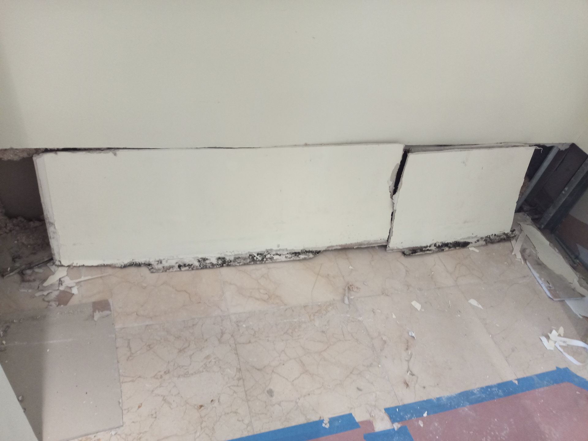 A broken wall is sitting on a tiled floor next to a window.