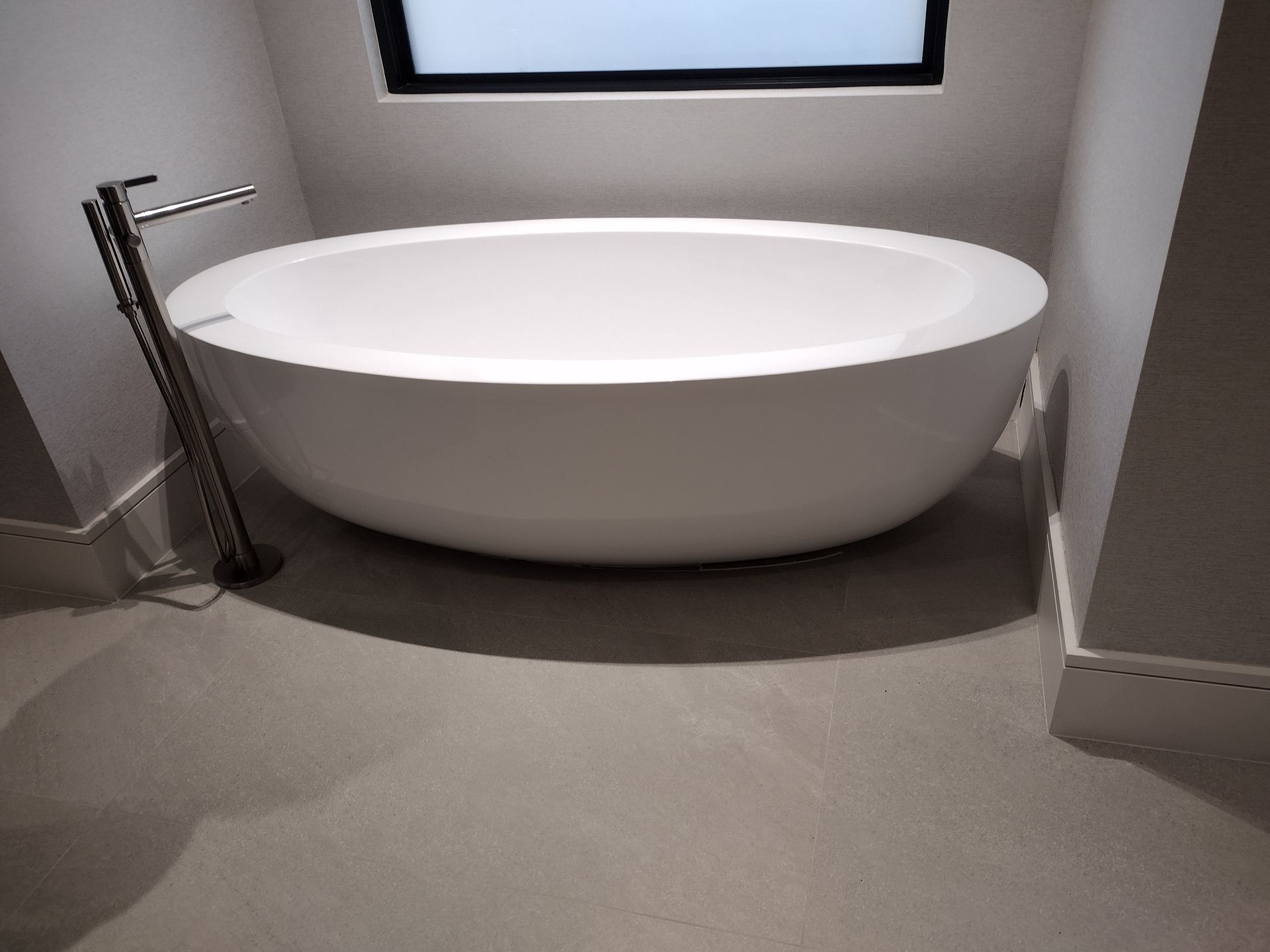 A large white bathtub is sitting in a bathroom next to a window.