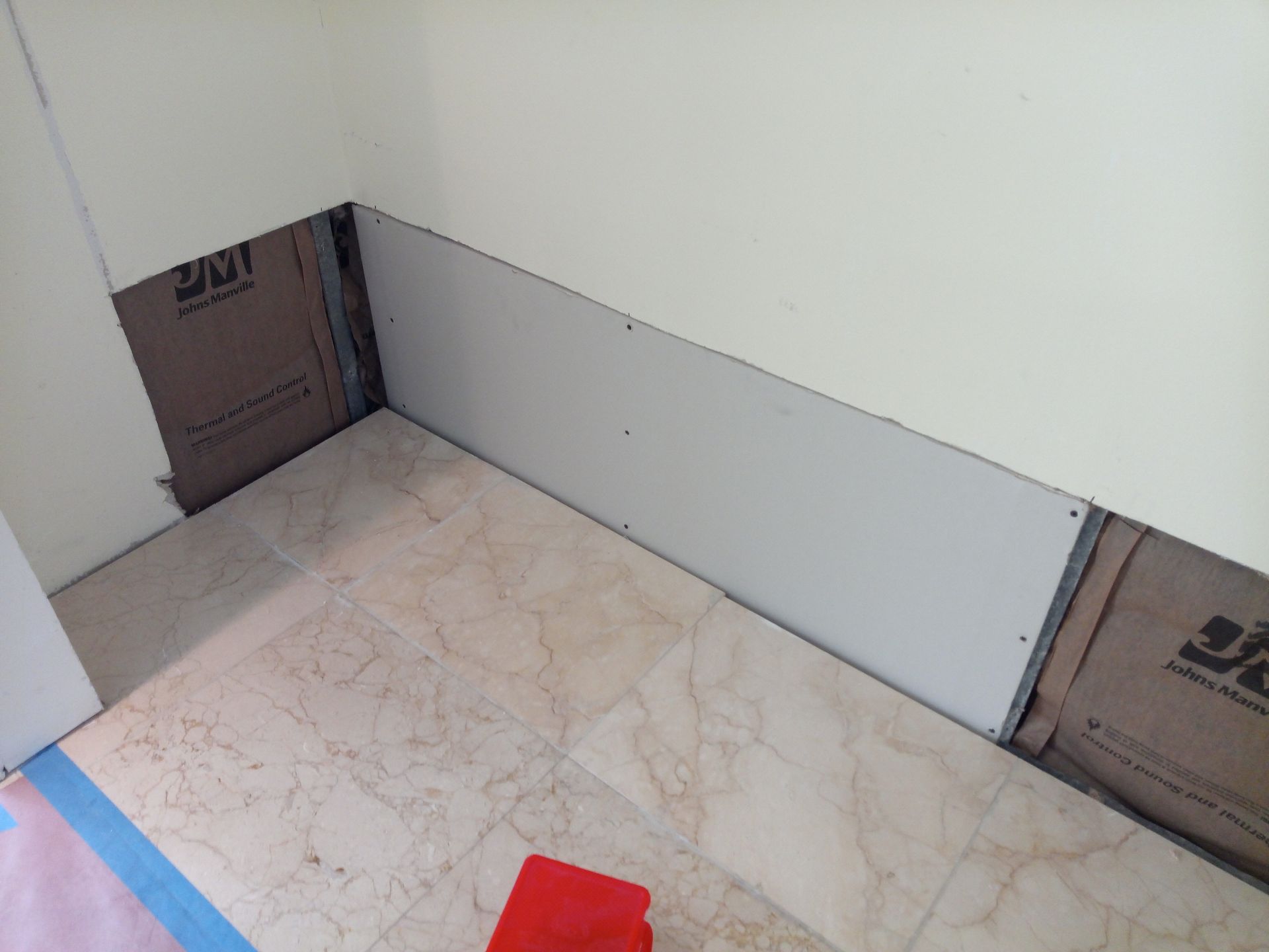 A corner of a room with a white wall and a marble floor.
