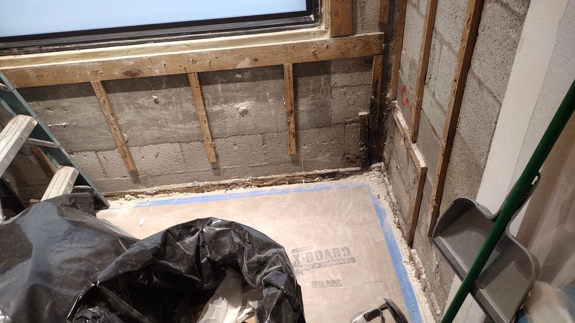 A room with a ladder and a trash bag on the floor.