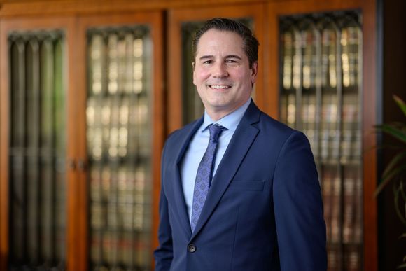 Sawicky in navy suit smiles in front of a wood-paneled bookcase.