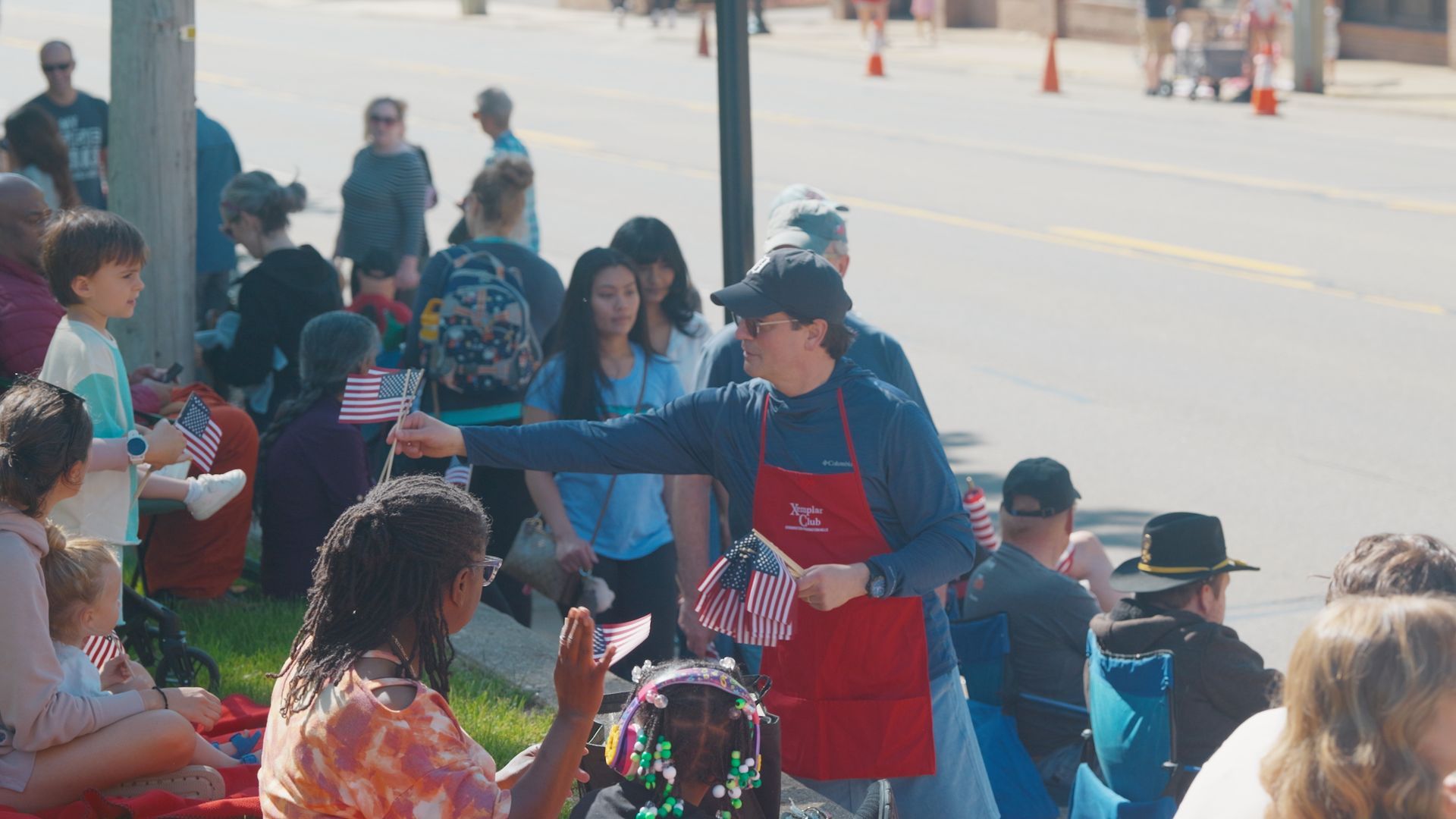 Michael Sawicky in the memorial day parade in Farmington Hills People gathered outdoors at a community event, with a volunteer in a red apron handing out items to a crowd.