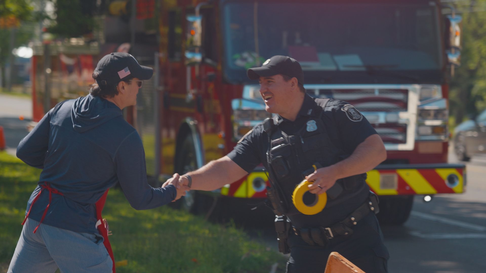 Michael Sawicky in the memorial day parade in Farmington Hills shaking hands with firefighters shake hands beside a fire truck, holding a yellow hose reel.