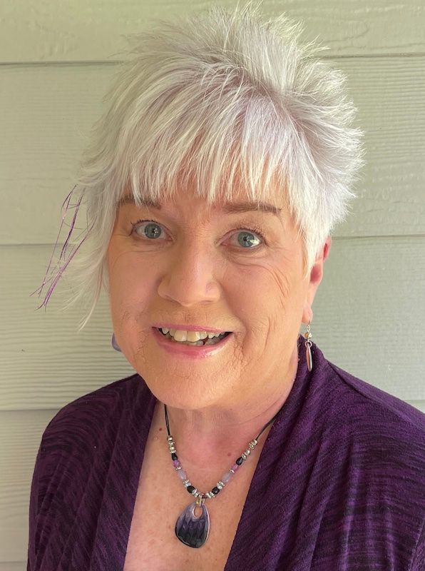 A woman with white hair is wearing a purple sweater and a necklace.