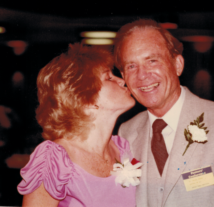 A woman in a purple dress kisses a man in a suit