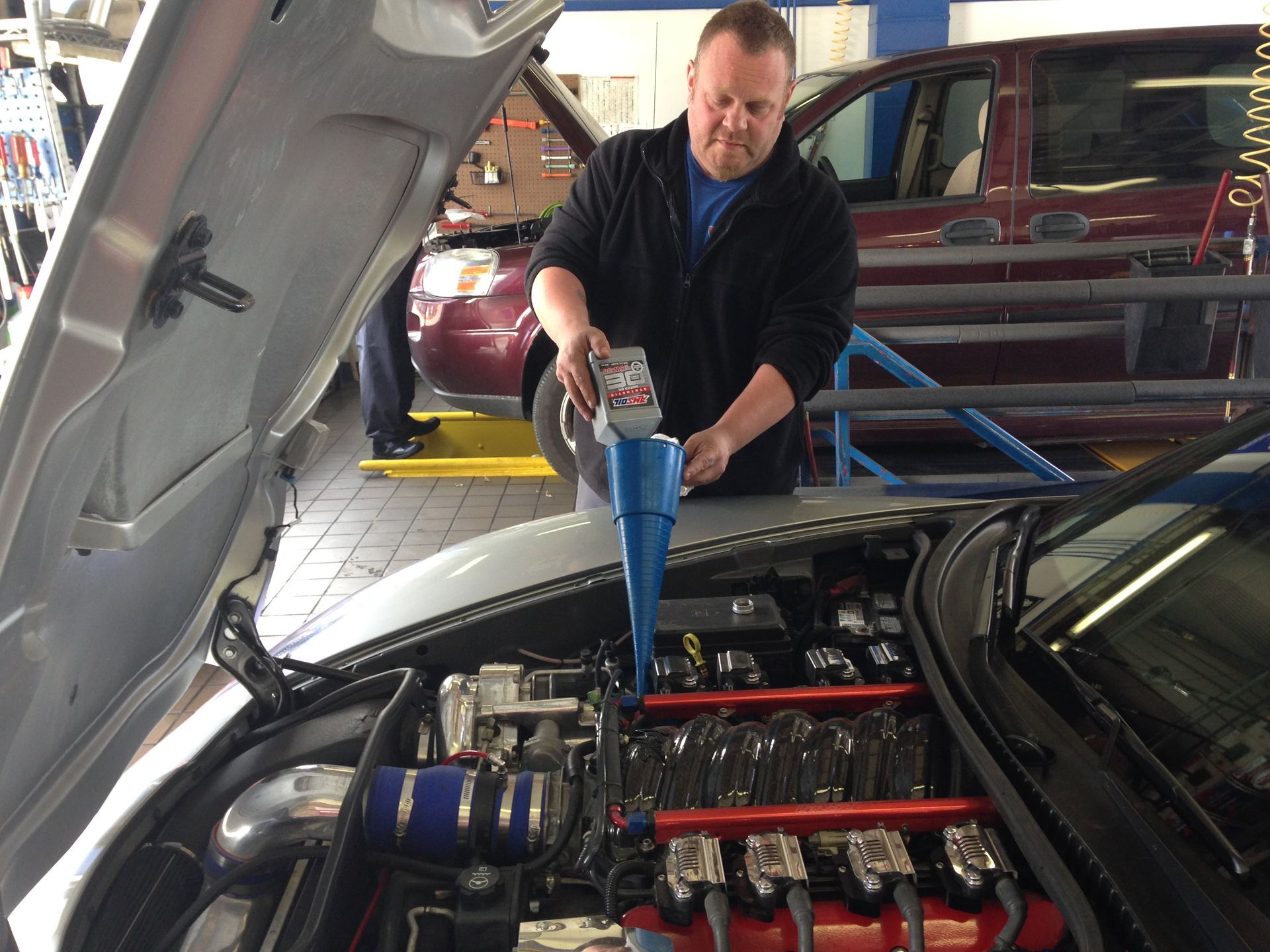 Mechanic pours oil into a car engine with a funnel in a repair shop.