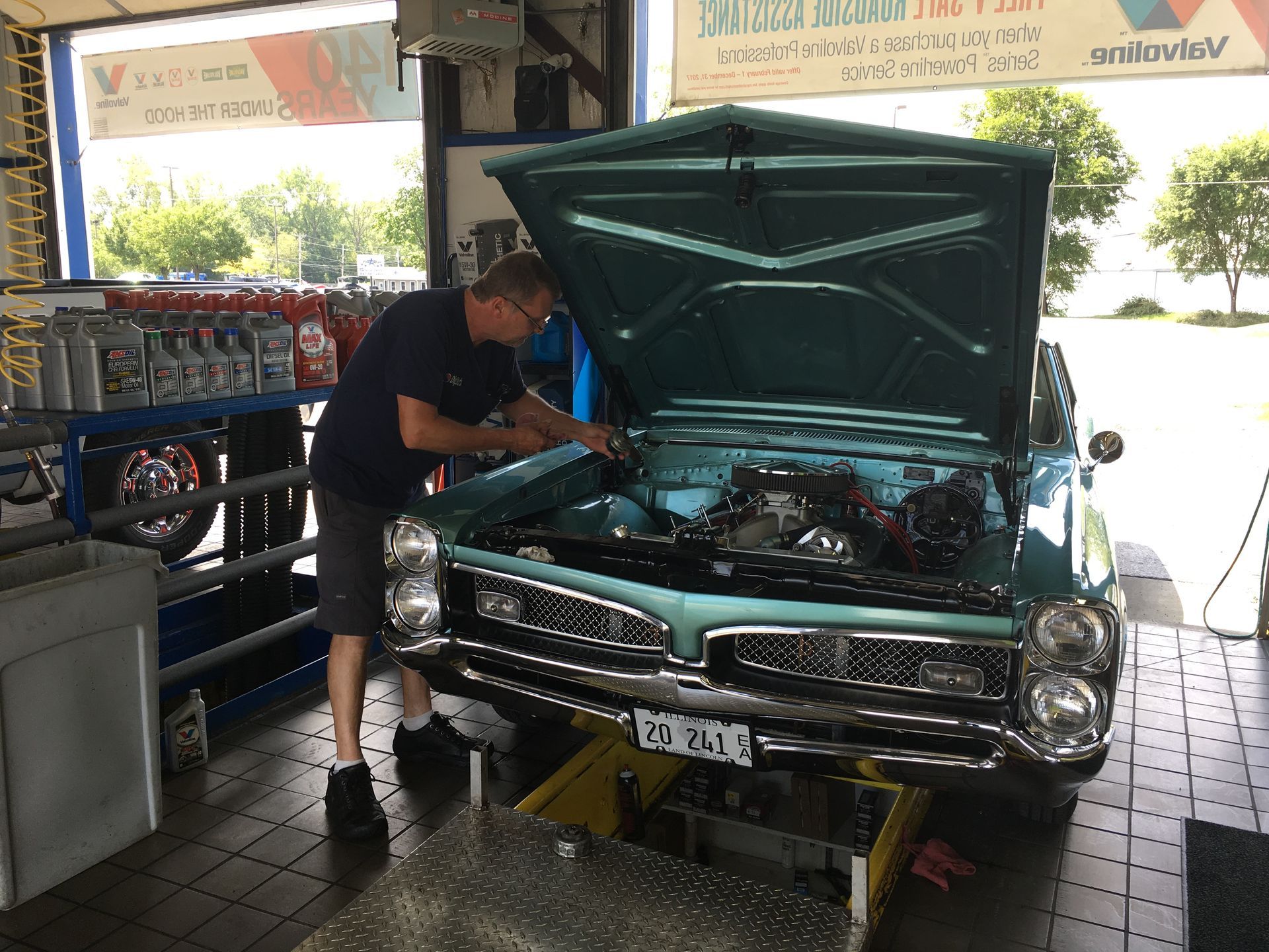 Man working on a classic teal car in a garage, hood open.