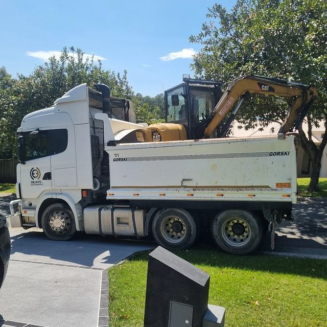 A white dump truck with a cat excavator on the back