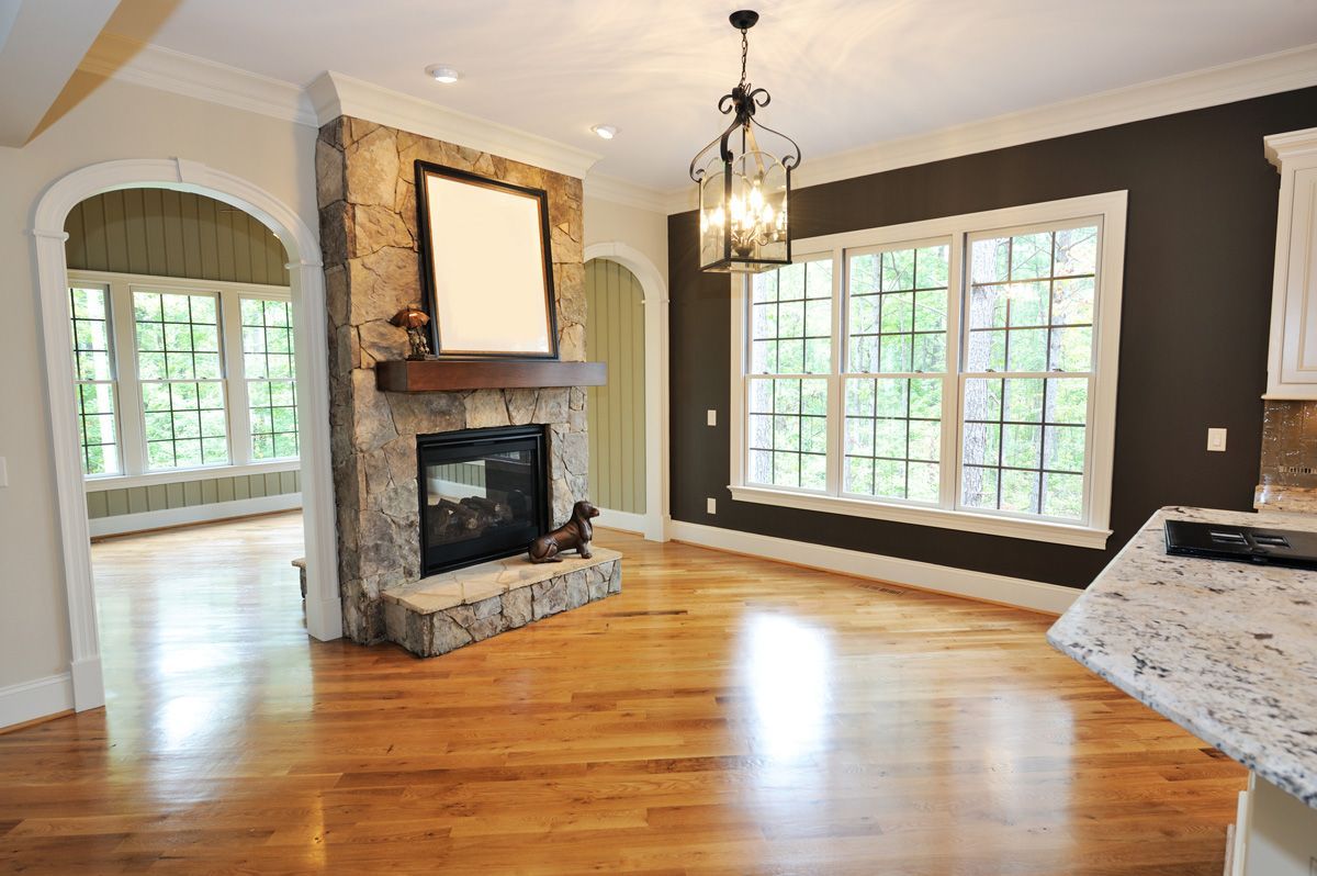 Bright interior with stone fireplace, hardwood floor, dark walls, and large windows.