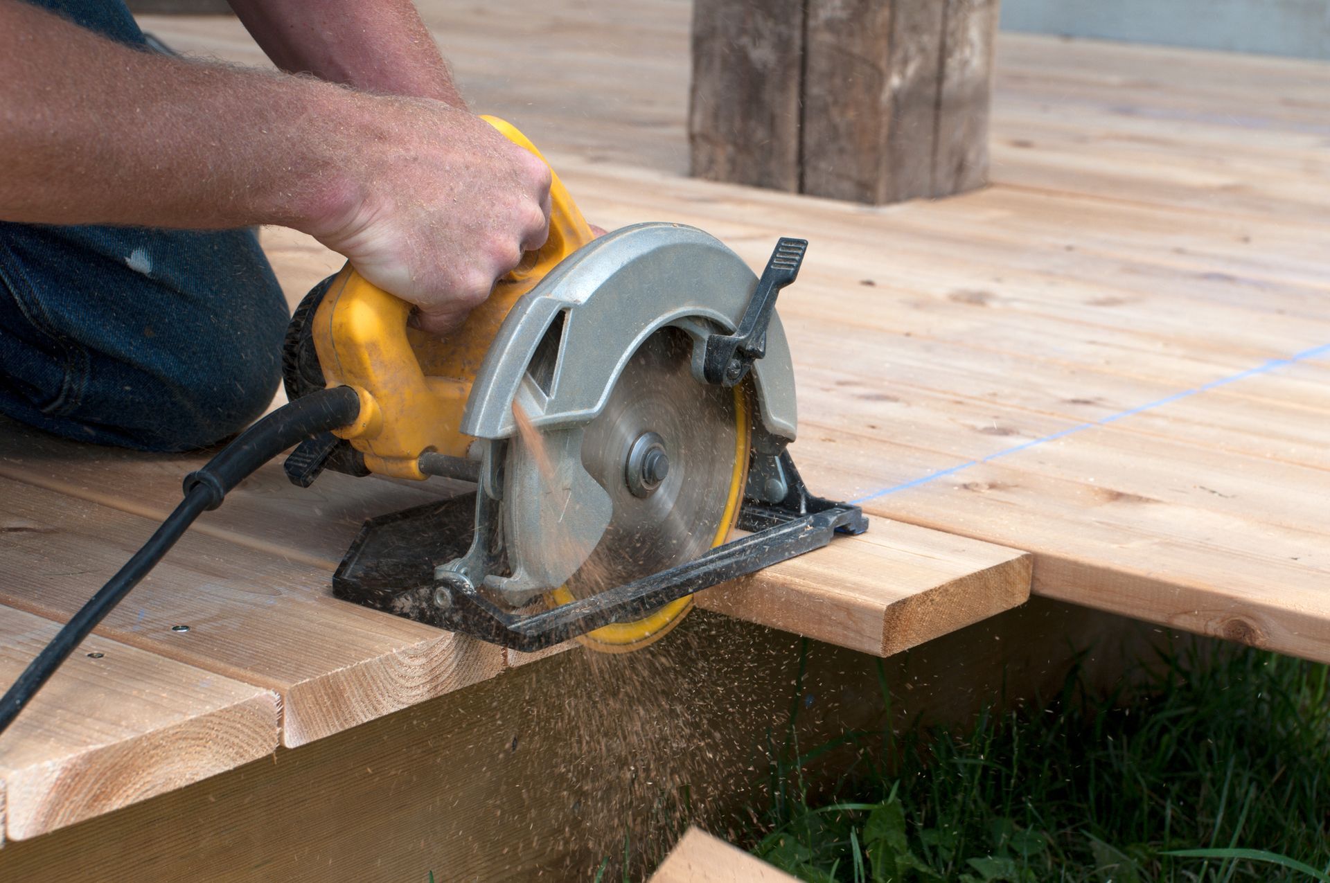 Person using a circular saw to cut a wooden plank on a deck, sawdust flying.