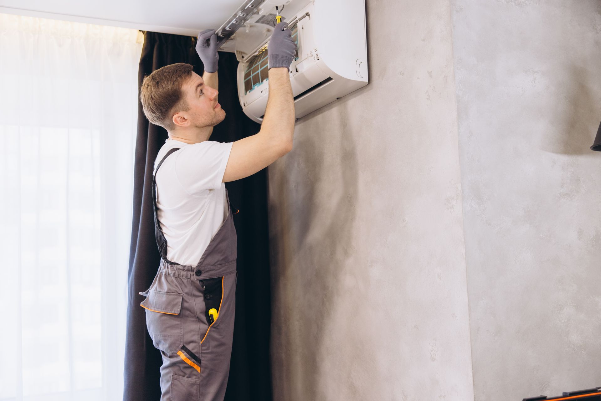 An air conditioning contractor repairing an air conditioner unit on the wall.
