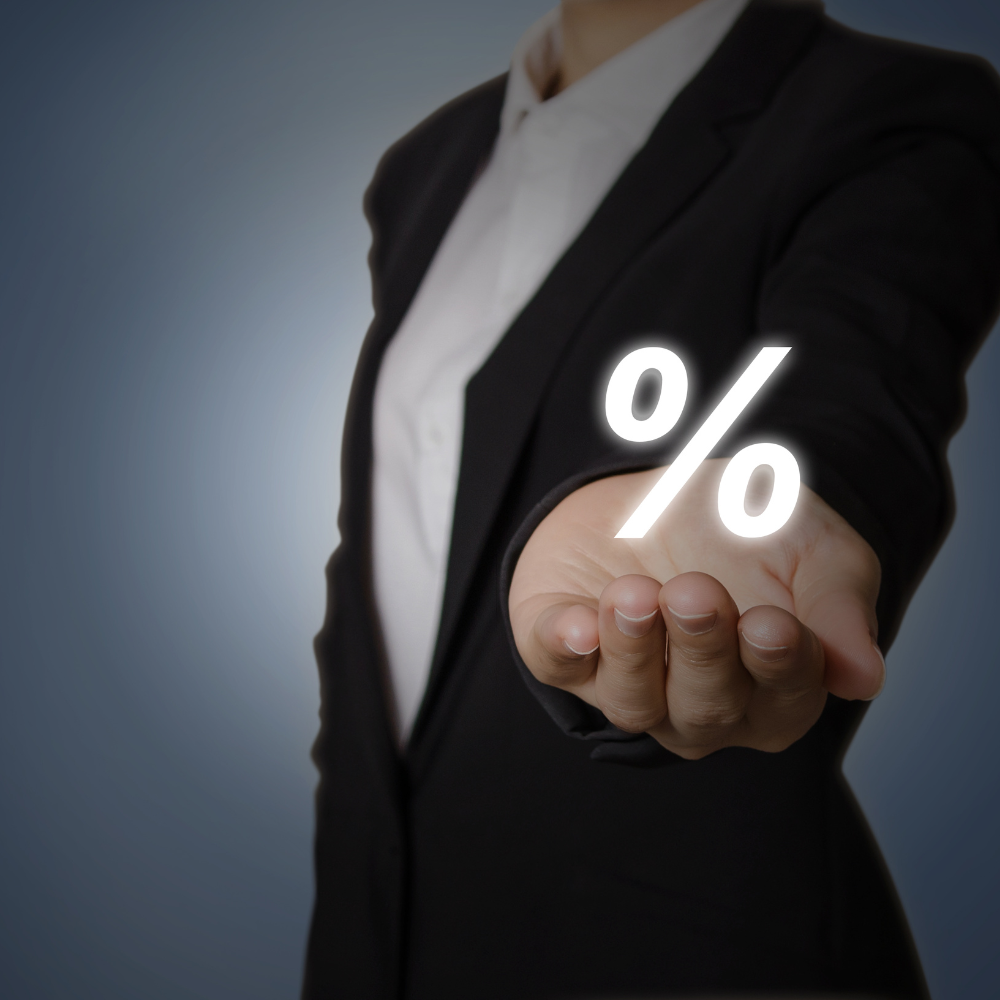 Eine Frau im Anzug hält ein Prozentzeichen in der Hand