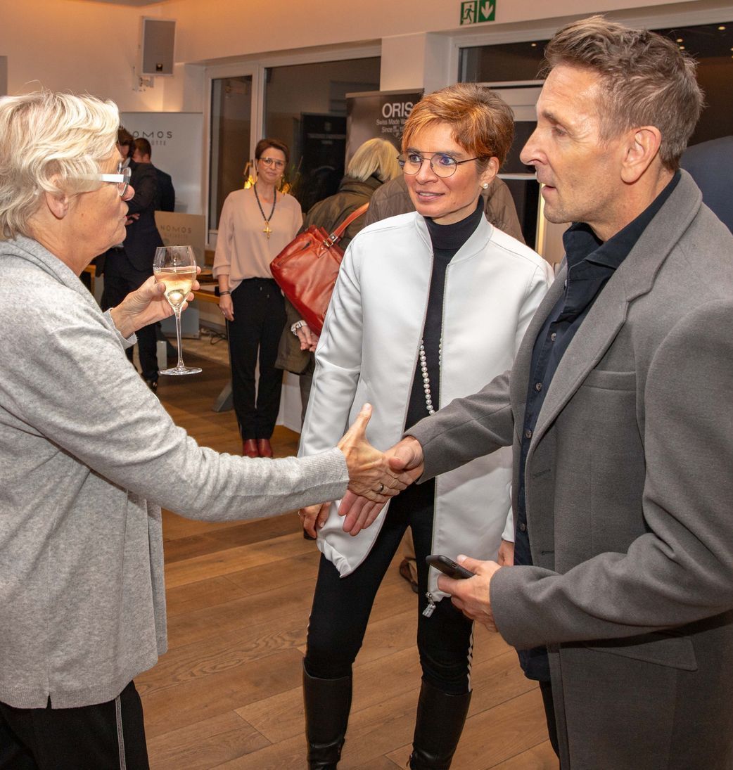 Ein Mann im Anzug schüttelt einer Frau in einer weißen Jacke die Hand