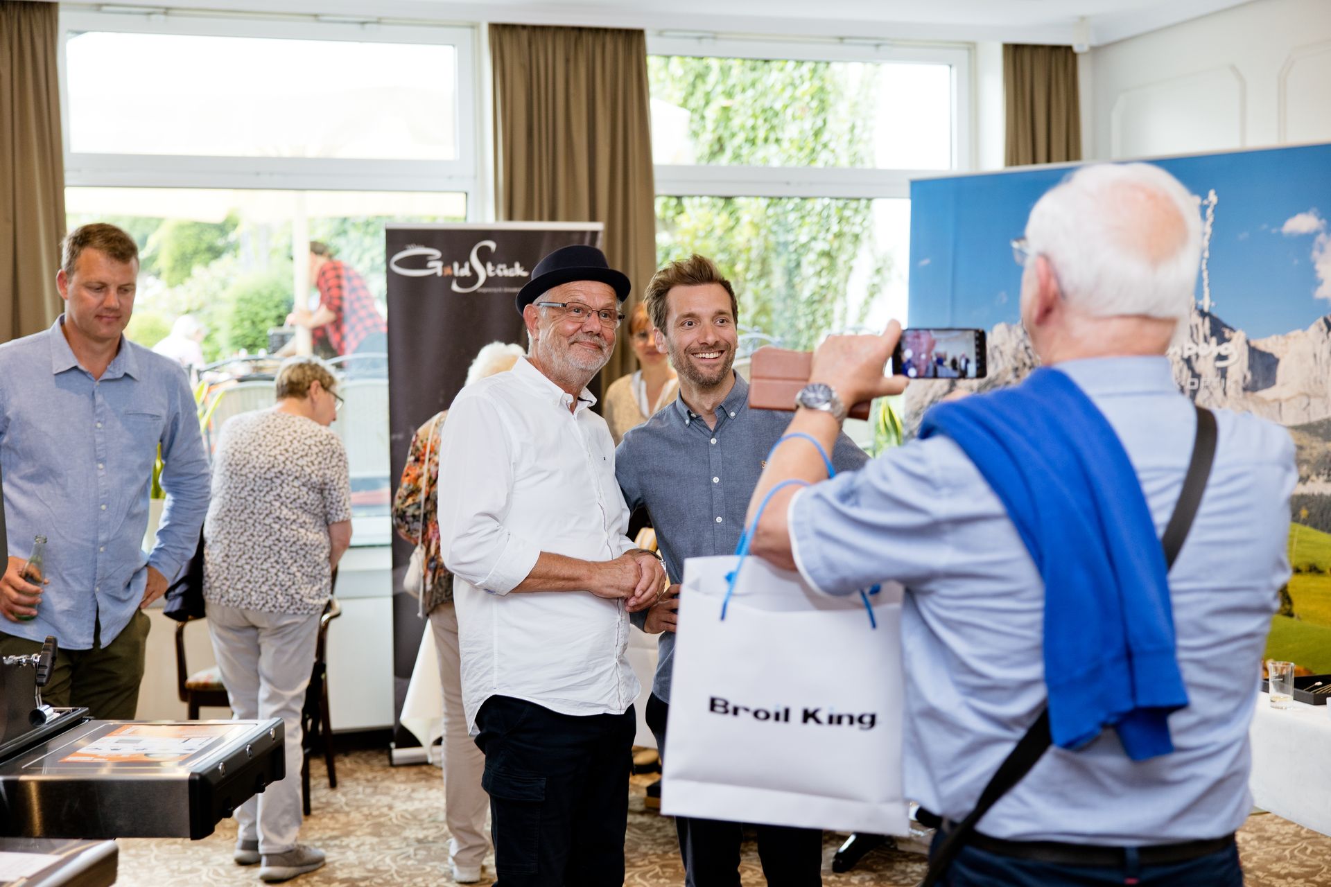 Ein Mann macht ein Foto von einer Gruppe von Menschen vor einem Schild mit der Aufschrift „Gruss“