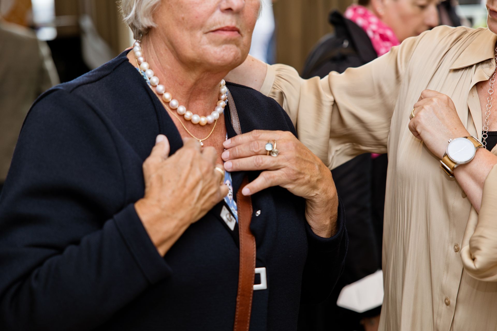 Eine Frau mit einer Perlenkette richtet ihre Jacke