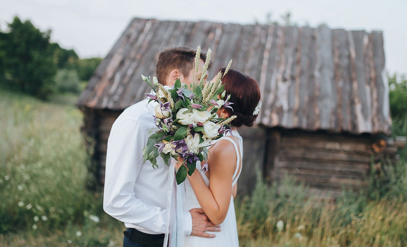 Eine Braut und ein Bräutigam küssen sich vor einem Holzgebäude.
