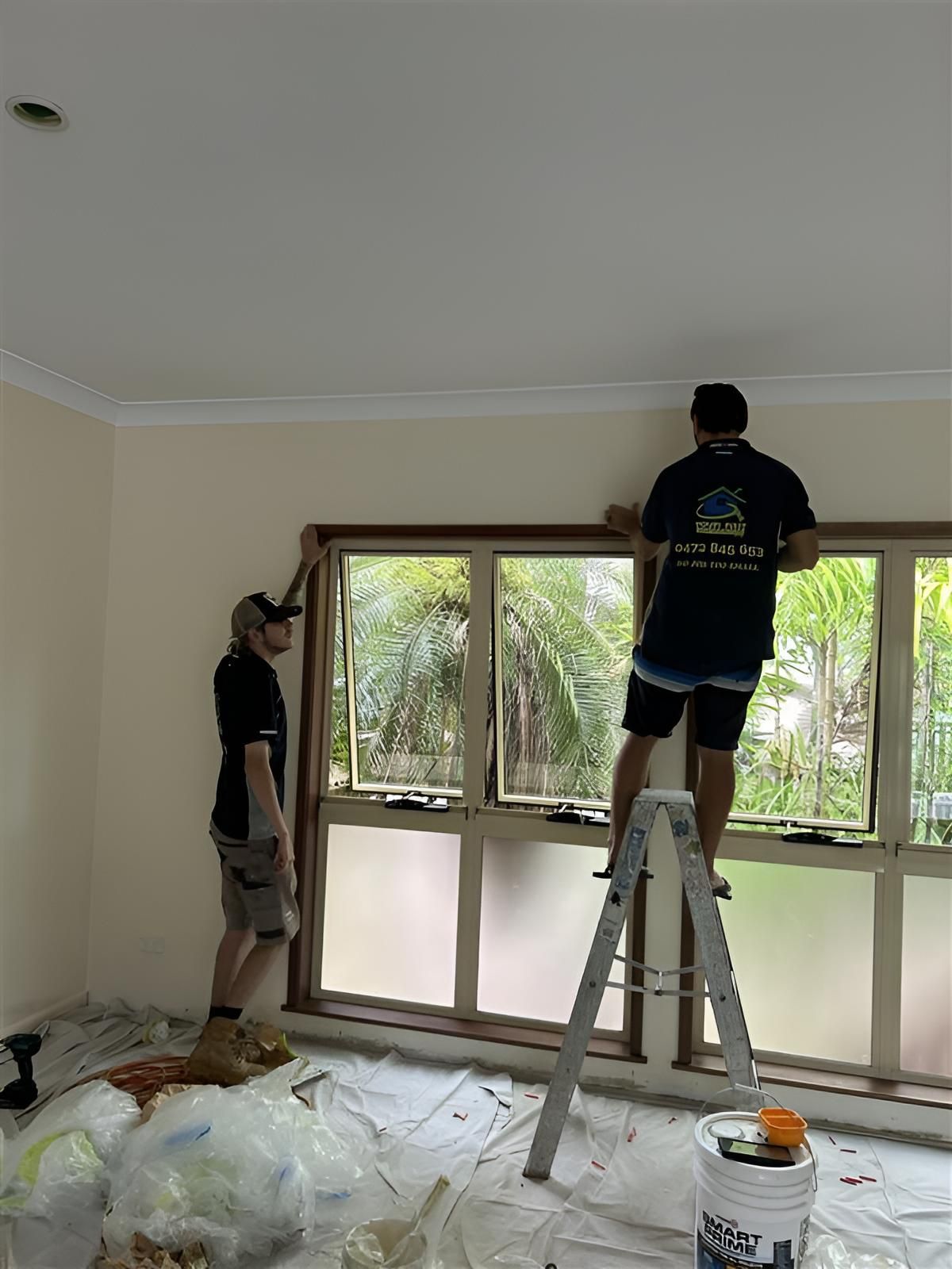 Two Men Are Working on a Window in a Room — Youfi Fixit Handyman Services in Edmonton, QLD
