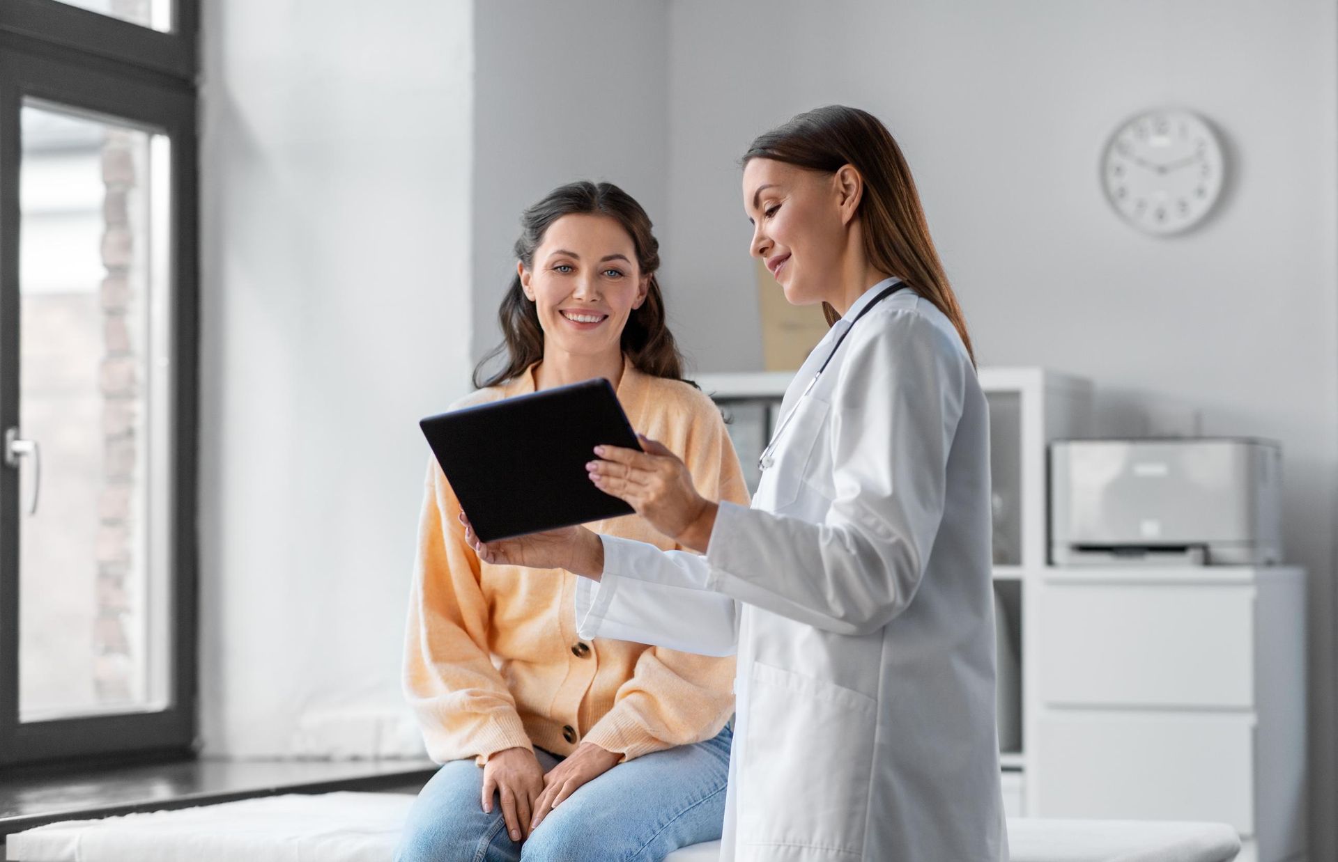 Female doctor shows tablet to smiling patient in light office.