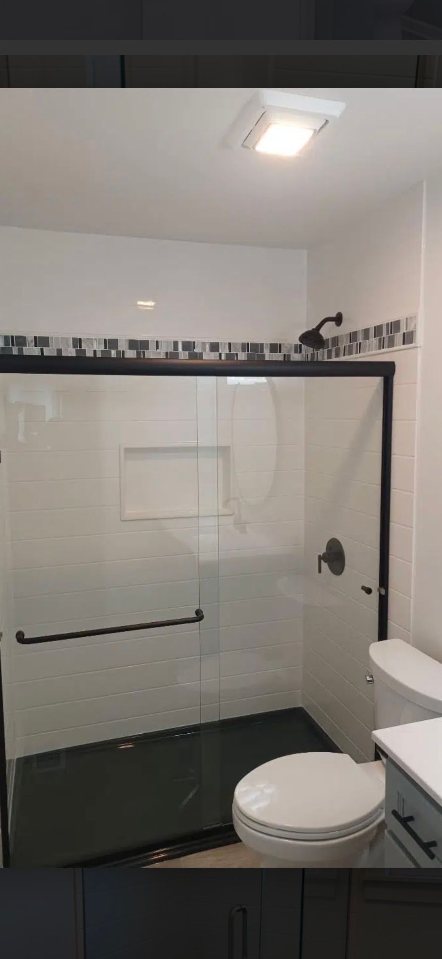 Bathroom with a glass shower, black fixtures, and a white toilet. Dark gray cabinets are visible.