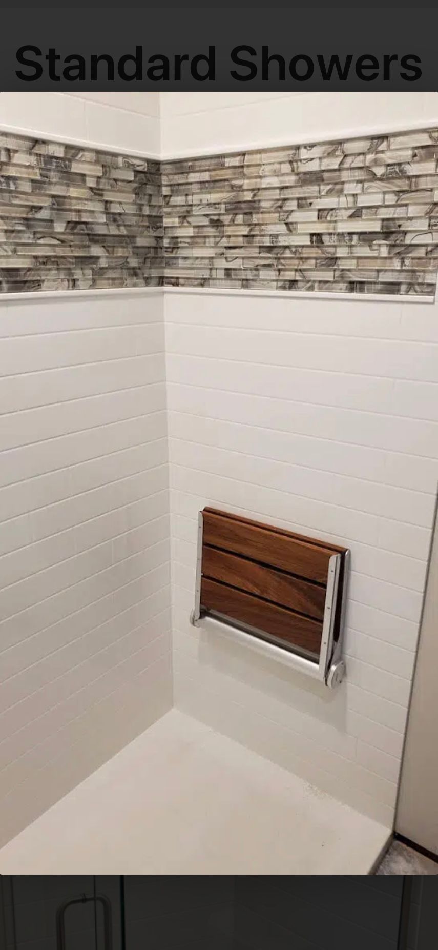 A shower with white tile walls and a wooden fold-down seat.  The wall behind the seat has a stone-like texture.