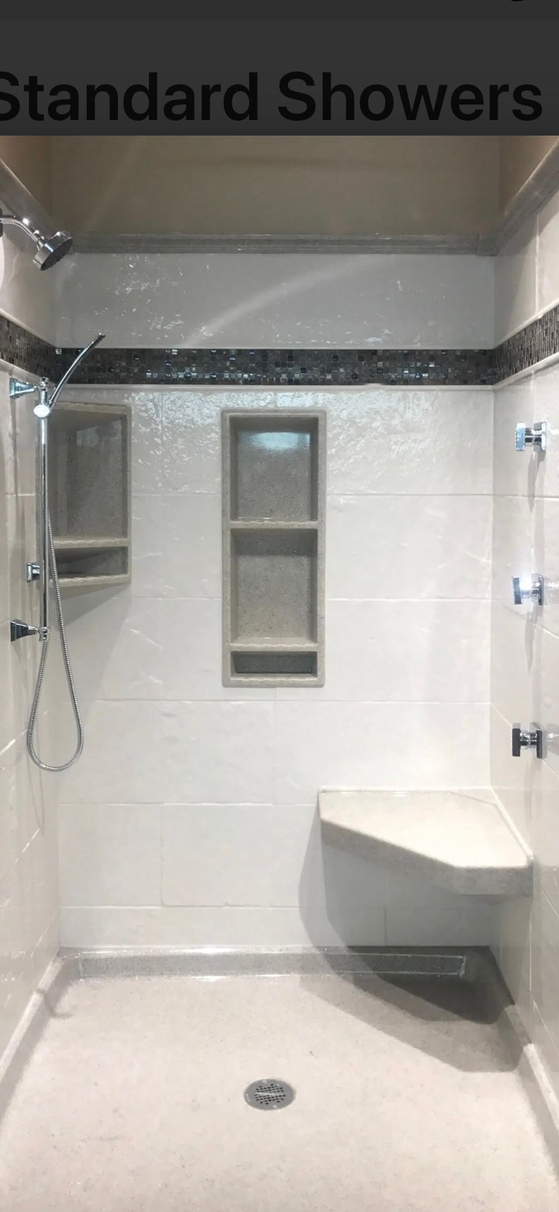A white tiled shower with a built-in bench, two niches, and a dark tile border.