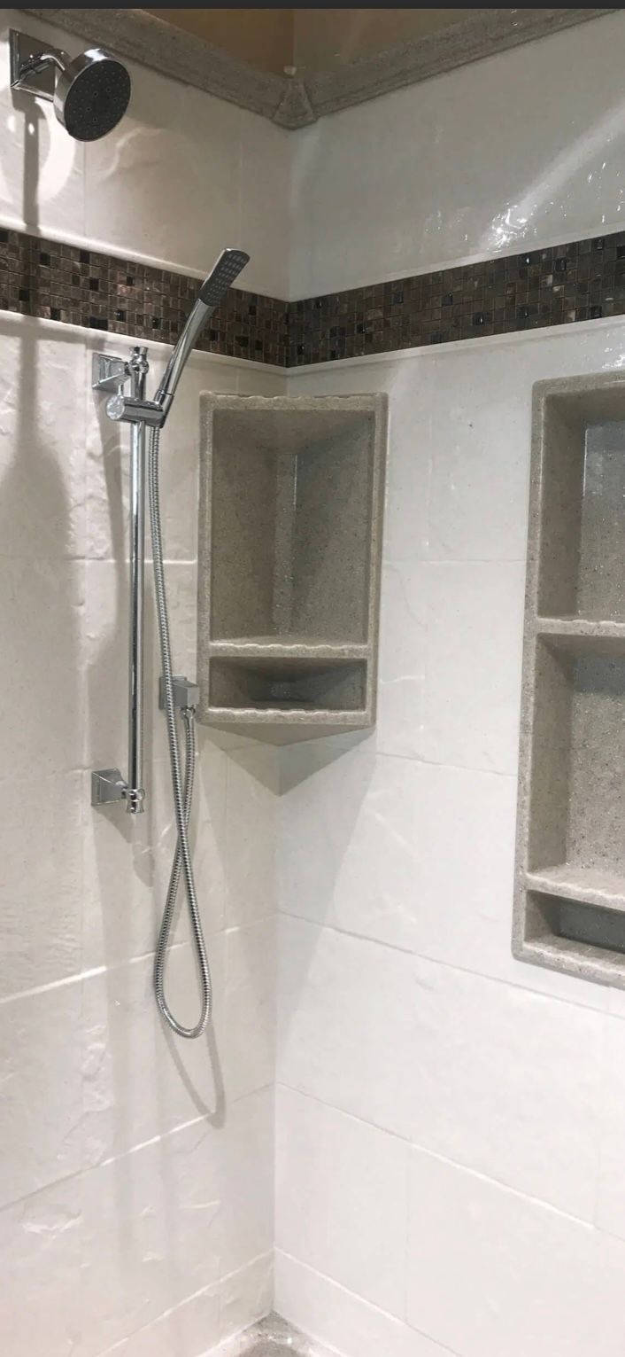 Shower with white tiled walls, shower head, handheld shower, and recessed shelf.