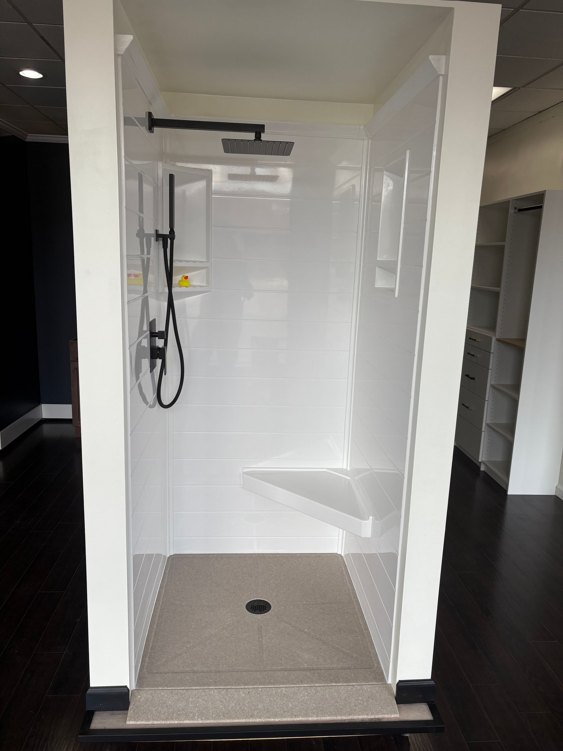 White shower stall with a built-in seat, a rain showerhead, and a handheld shower.