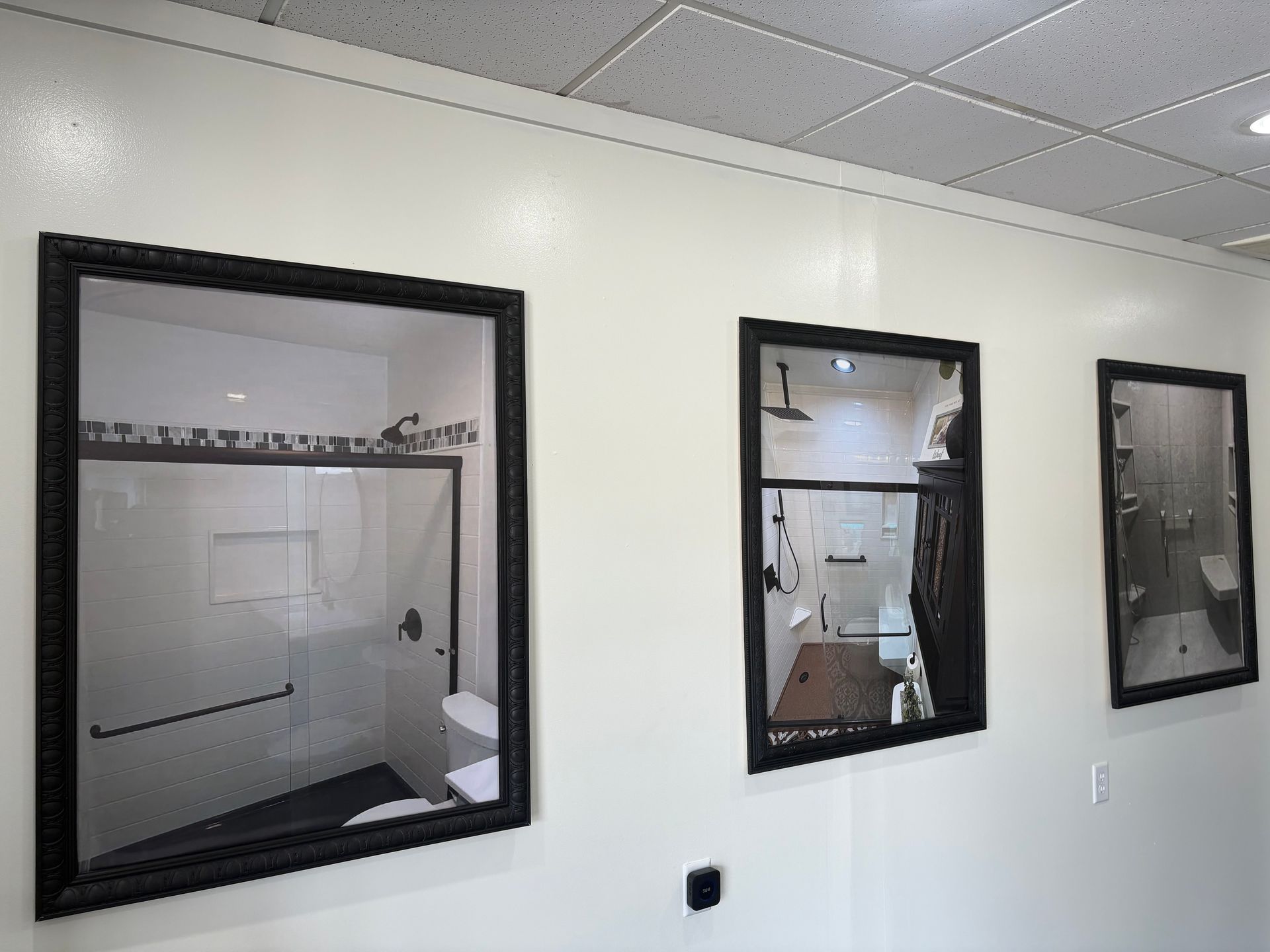 Three framed images of bathrooms hang on a white wall.