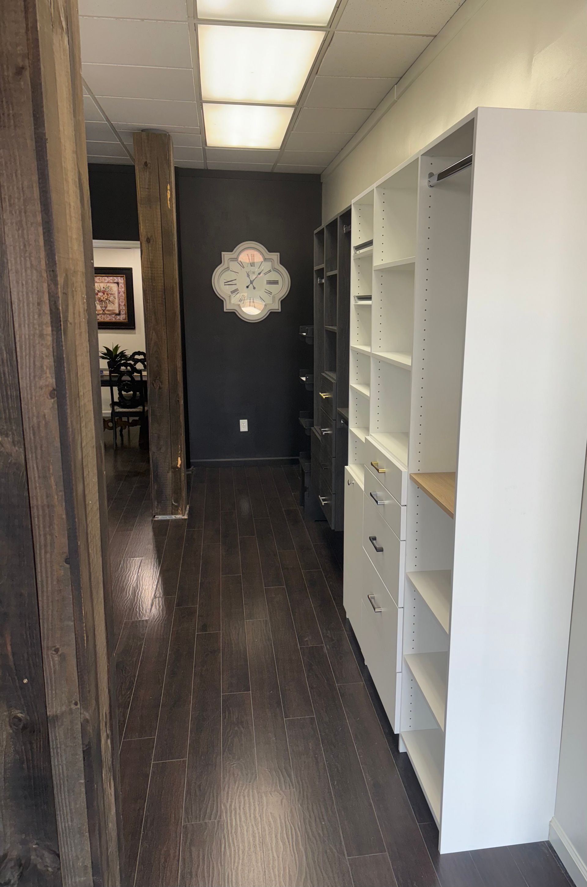 Hallway with dark wood floor, white shelves, dark gray wall with ornate decoration, and wood support beams.