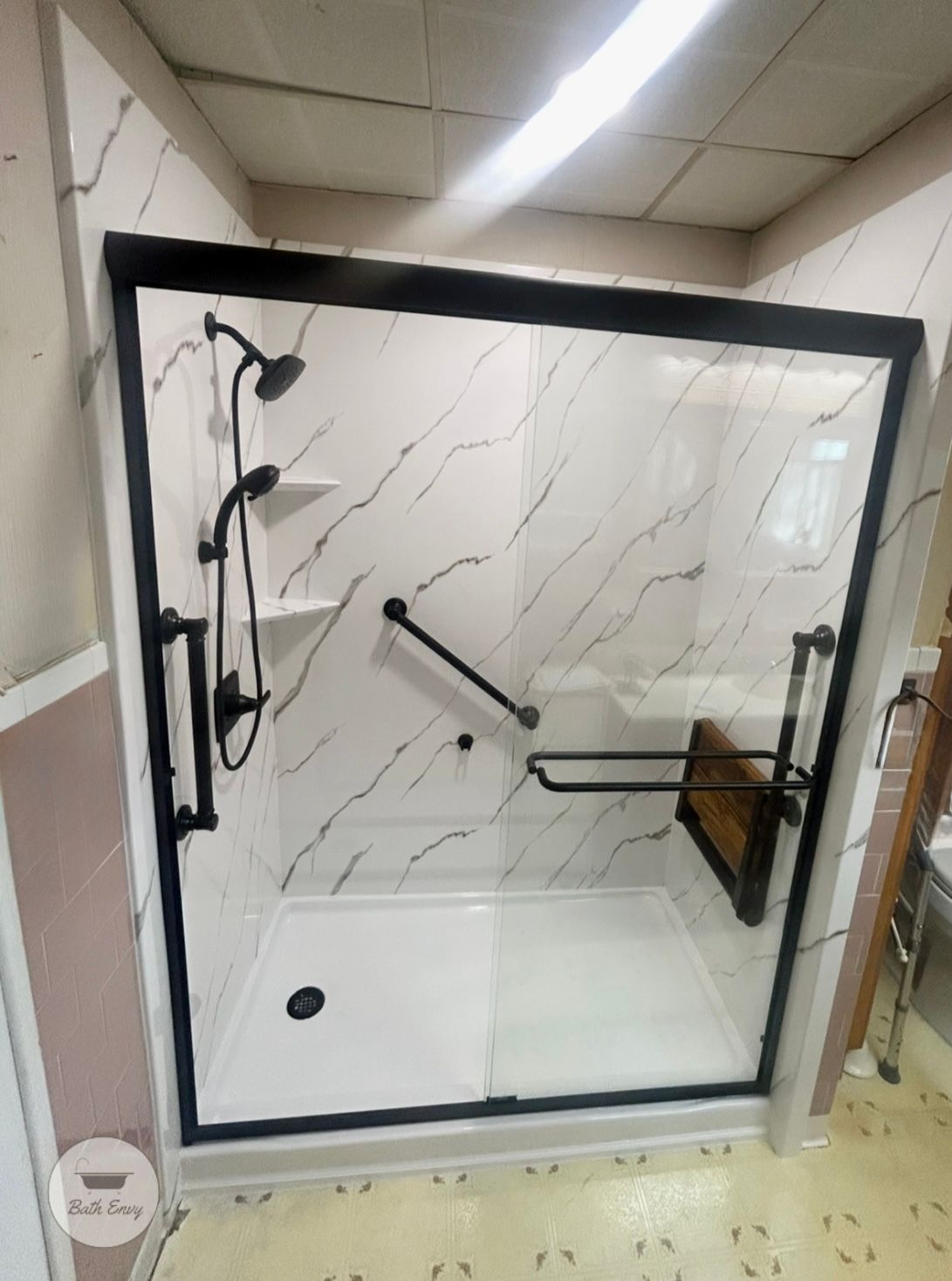 Black-framed shower with marble-look walls, black fixtures, grab bar, and built-in seat for accessibility.
