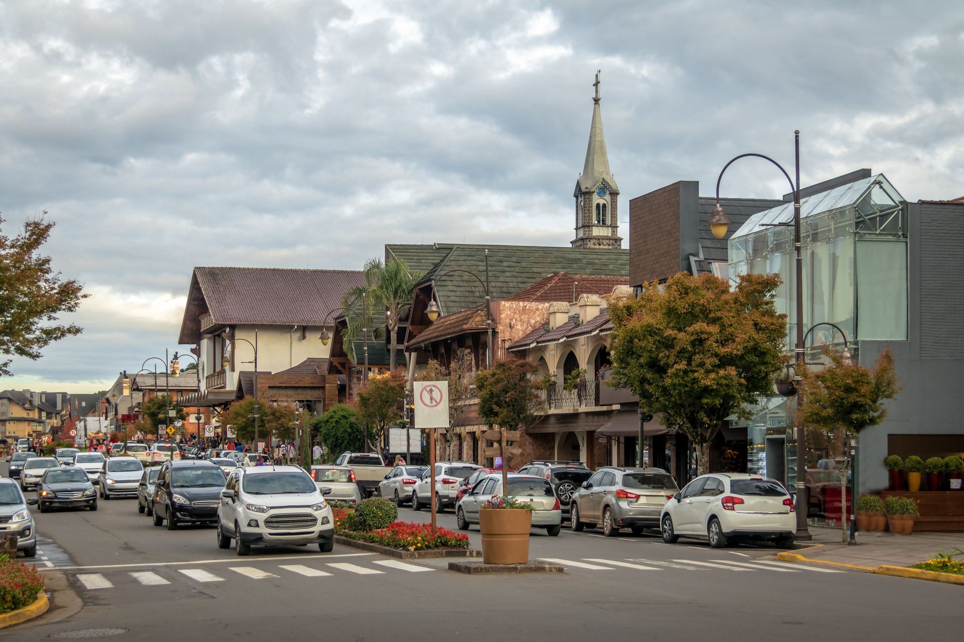 Street scene with buildings, cars, and a church steeple under a cloudy sky.
