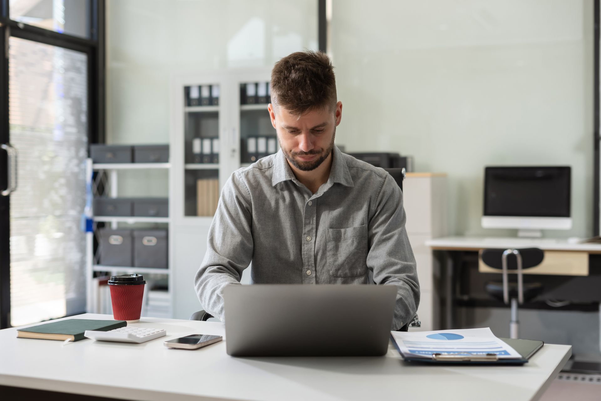 Man typing on laptop at a desk, office setting.