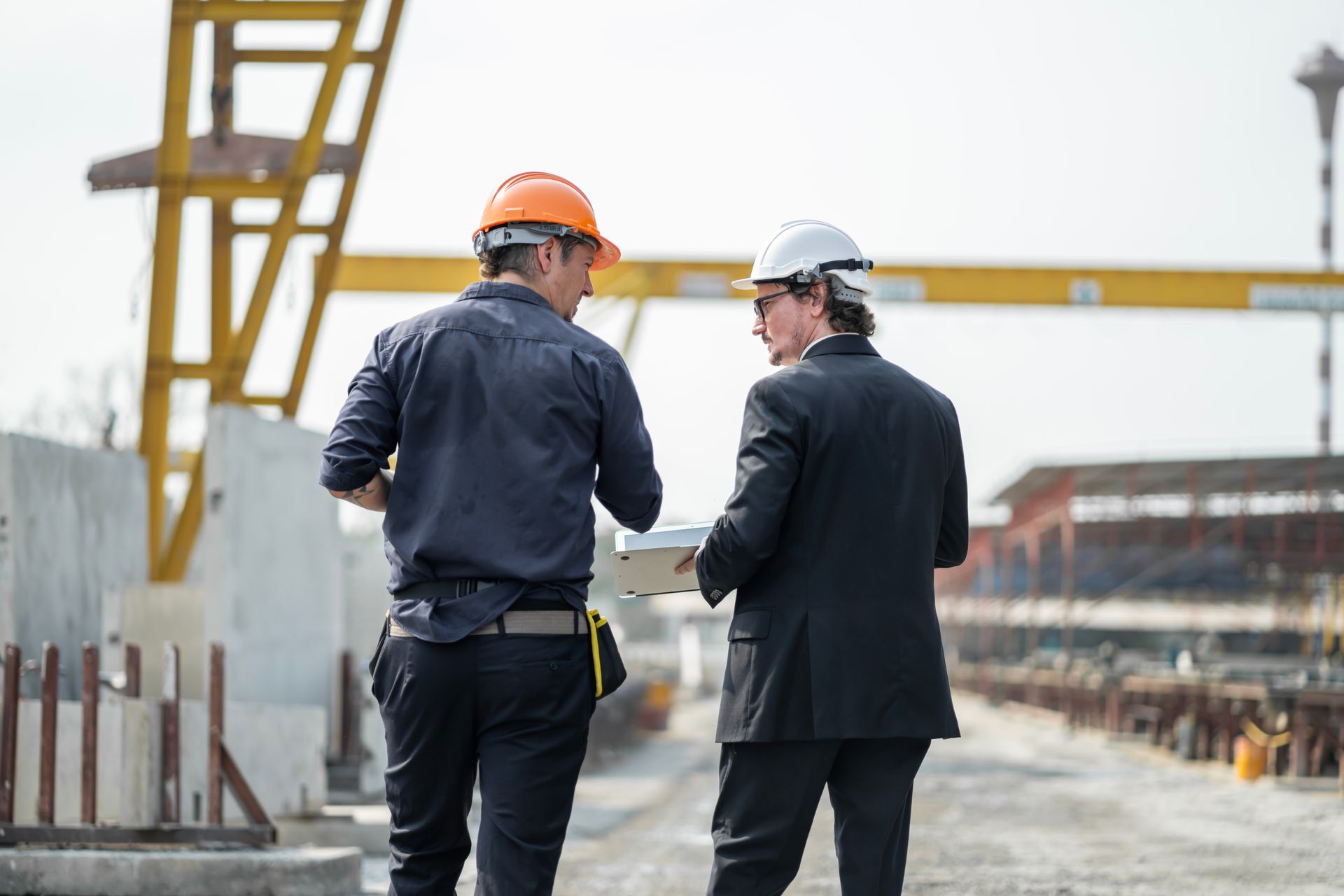 Two men in hard hats and work clothes discussing plans at a construction site.