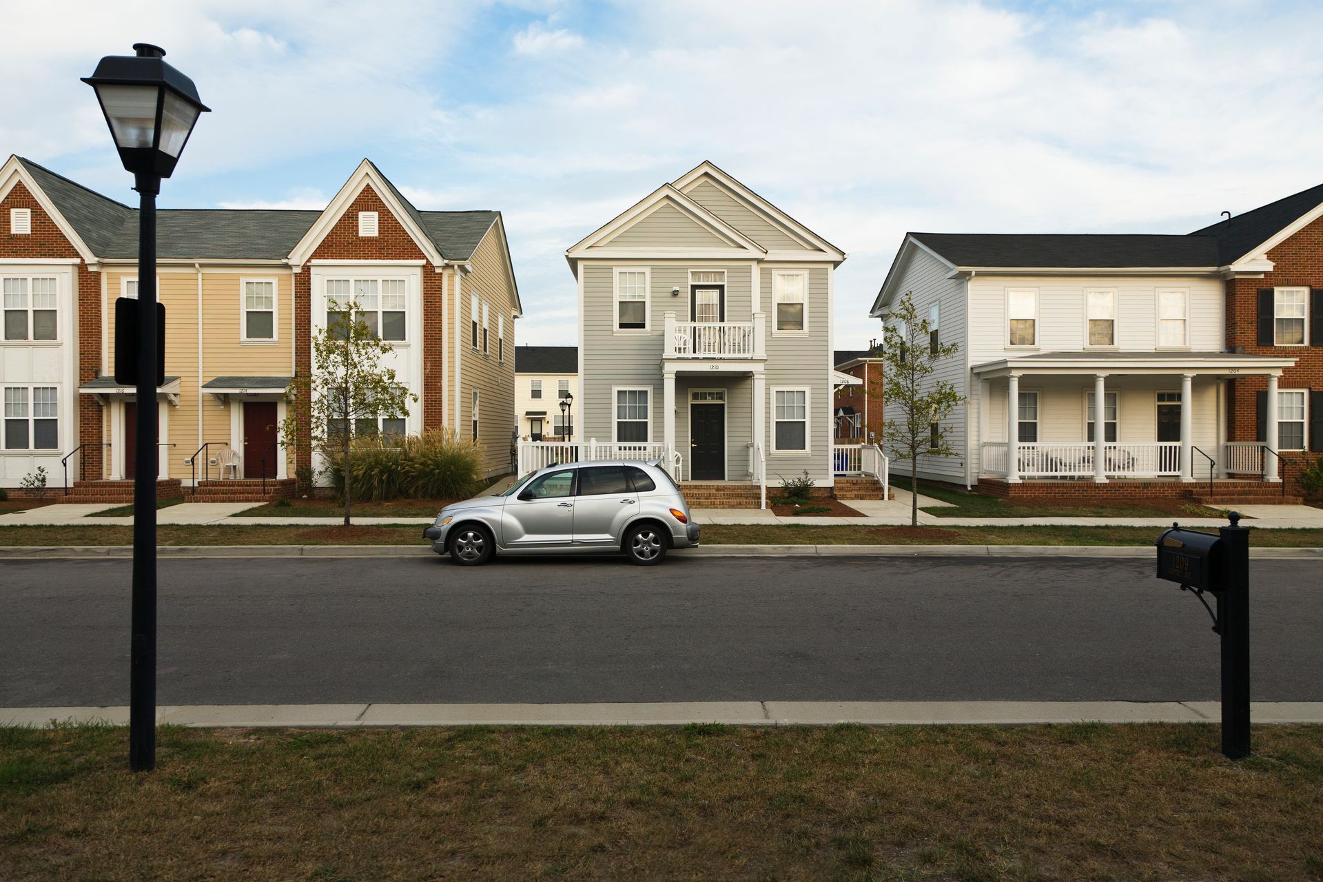 Row of suburban houses, silver SUV parked on street, black mailbox, lamppost, blue sky.
