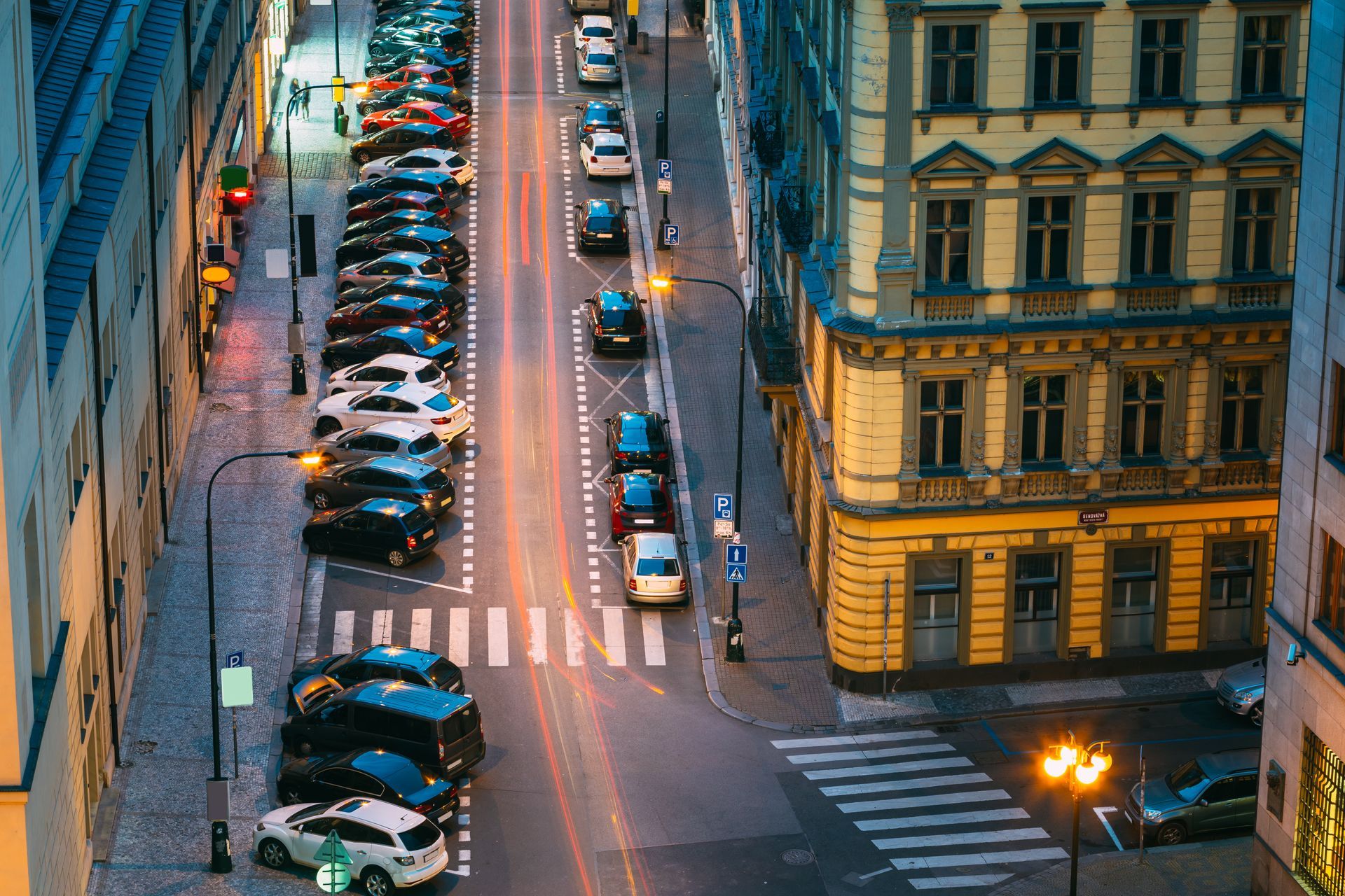 Cars parked on a narrow European street at dusk, with buildings on both sides.