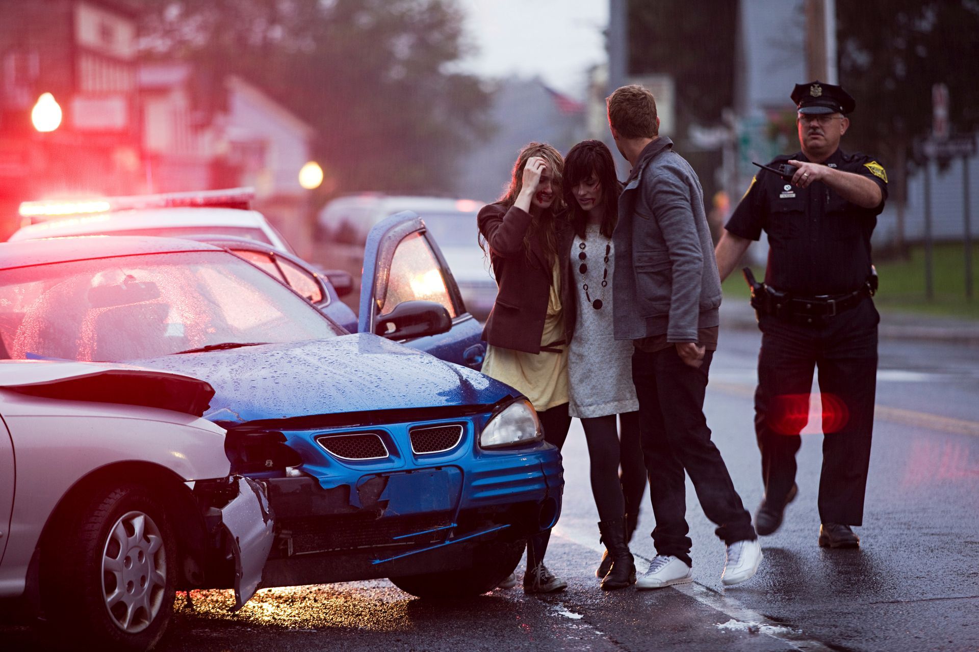 Car crash scene with damaged blue car, upset people, and a police officer pointing.